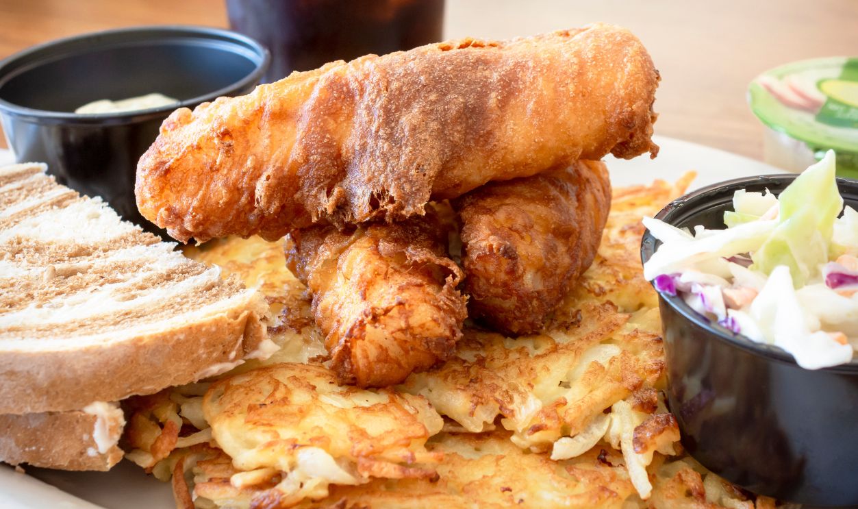 A traditional Wisconsin Friday night fish fry from a diner including deep fried cod, coleslaw, marbled rye bread, applesauce, cola, tartar sauce and hash browns.
