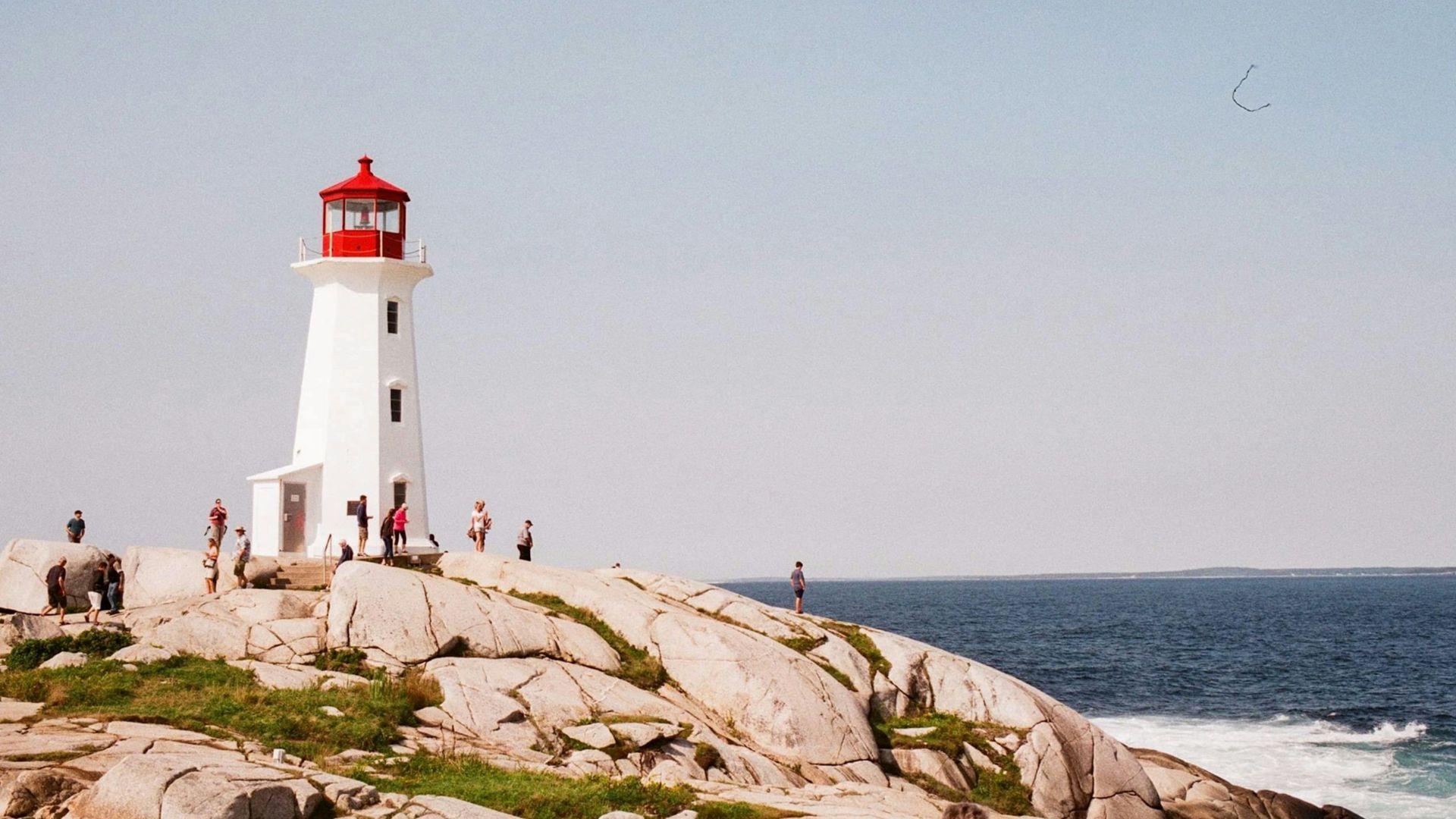 white and red lighthouse on brown rocky shore under blue sky during daytime