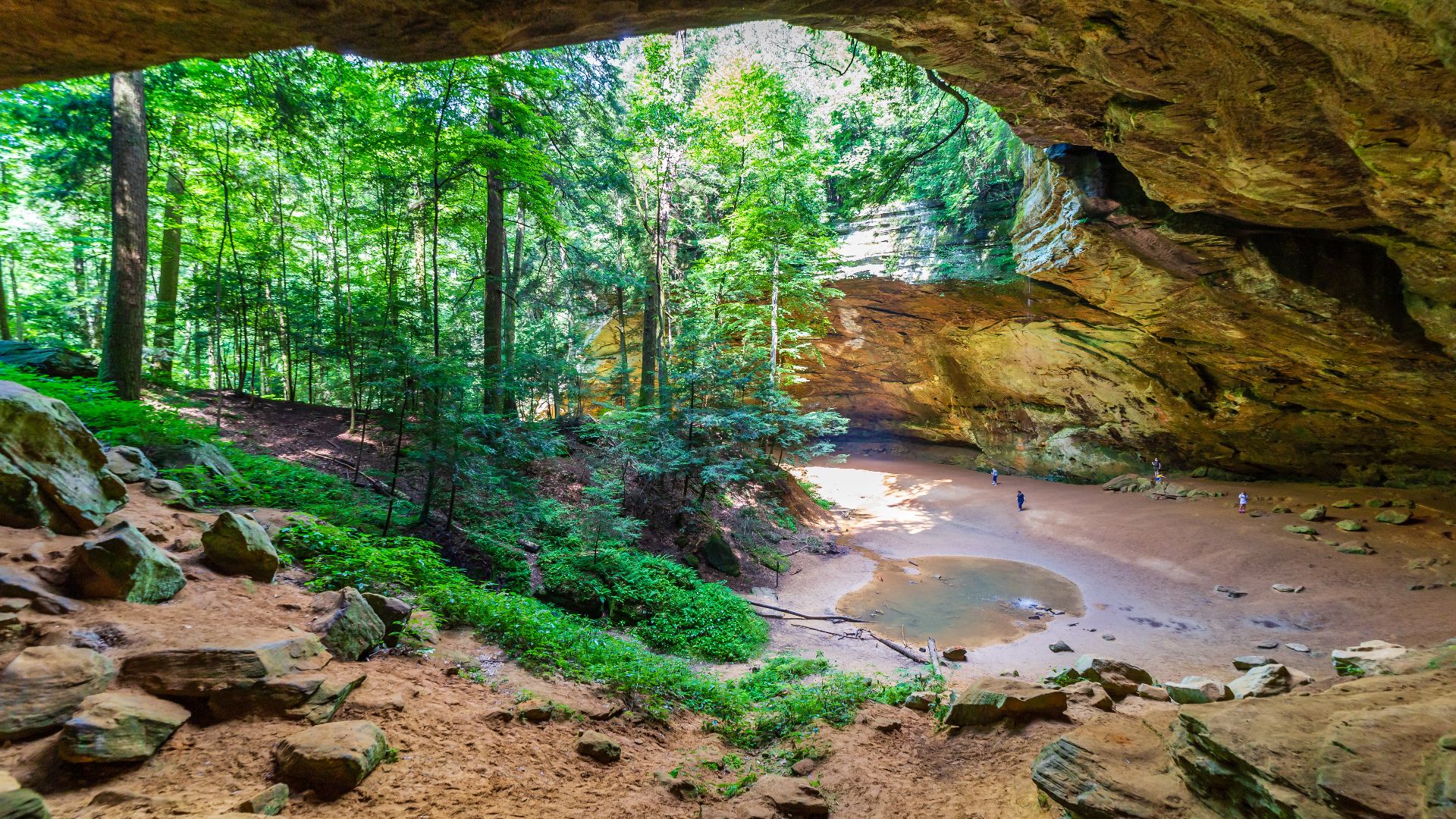 The impressive size of Ash Cave makes it one of the gems of Hocking Hills State Park in Ohio. The magnitude of the rock formation is spectacular to behold, and highlighted in a photo by the small size of people seen on the floor of the cave. Ash Cave is i