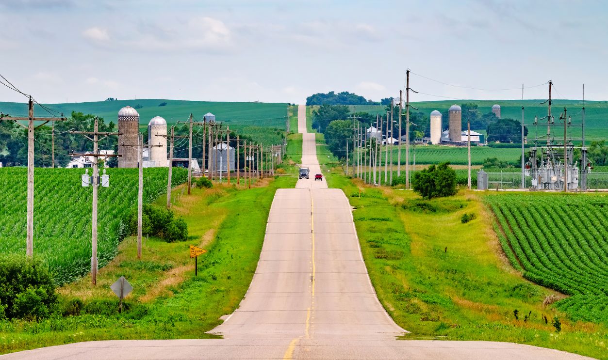Truck and car traveling in opposite directions on long paved road across hilly farmland in northeastern Nebraska, USA, on a cloudy morning in summer, for rural, agricultural, or regional themes
