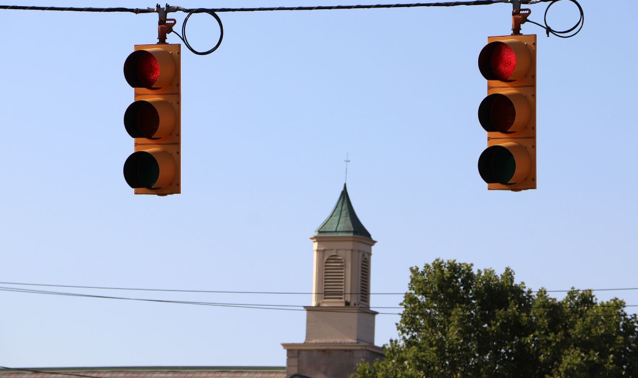 Low angle view of municipal traffic light signals suspended on overhead utility wires over a small town intersection crossroad.