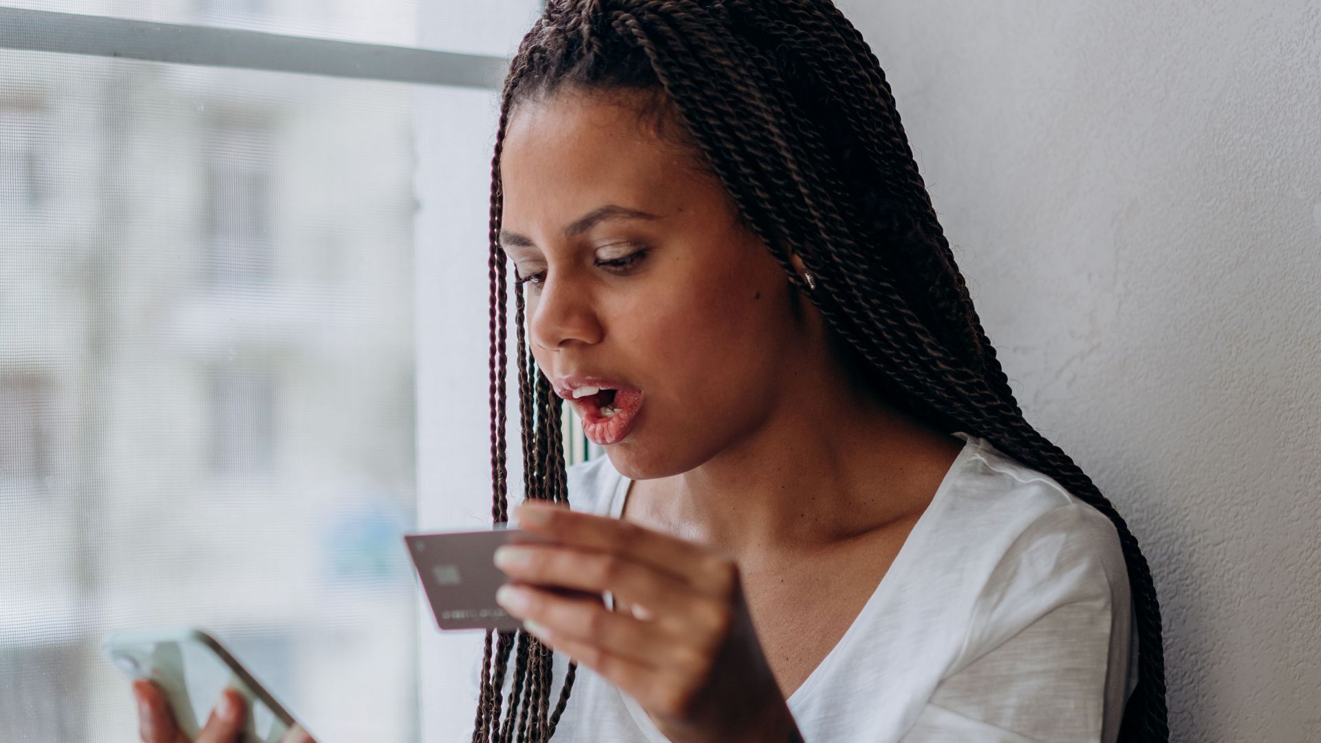African woman using smartphone and credit card at home.