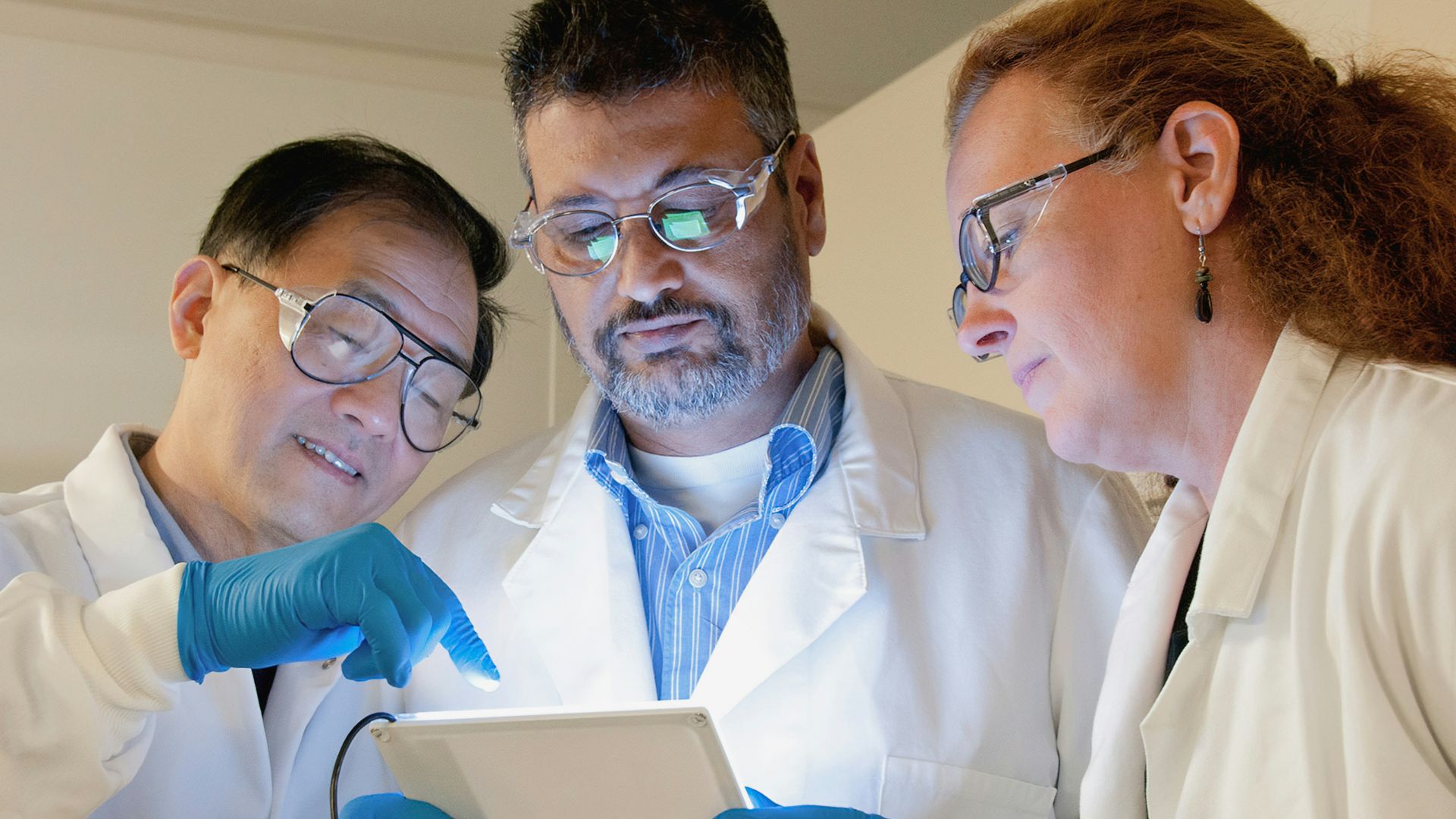 three people in lab coats looking at a tablet
