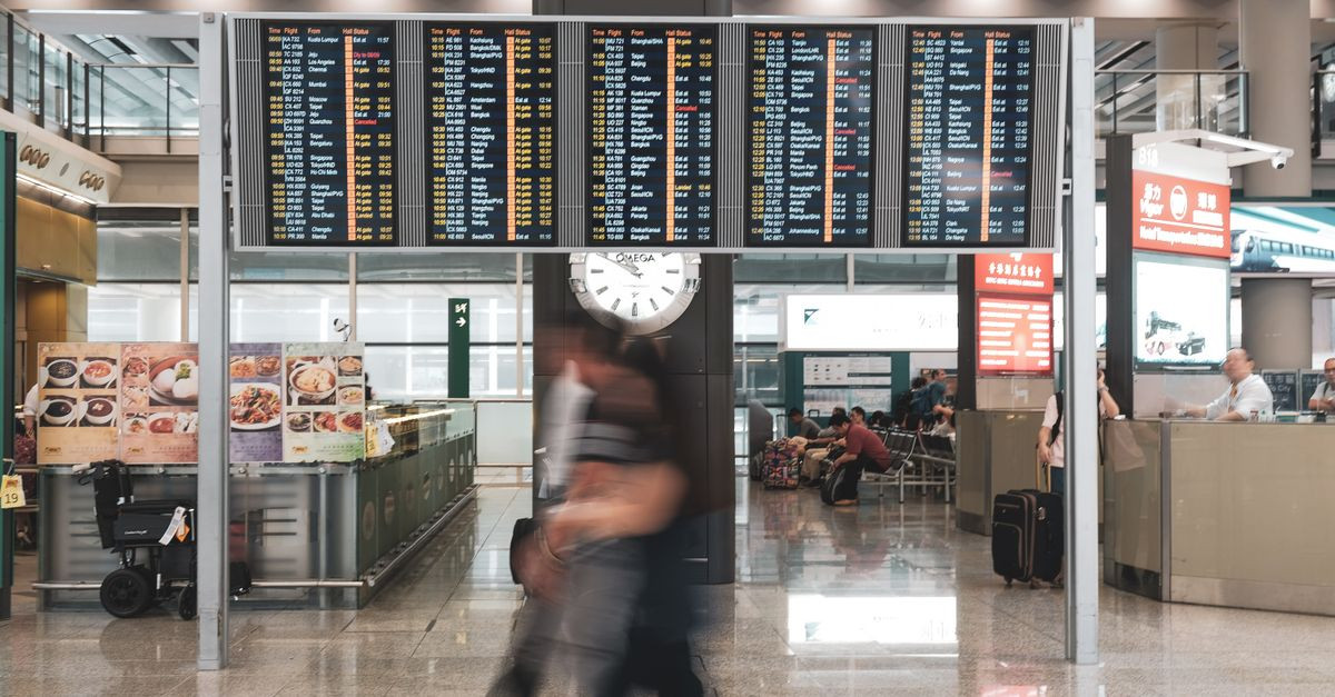 Blurred motion of travelers in a modern airport terminal with departure screens and a prominent clock.