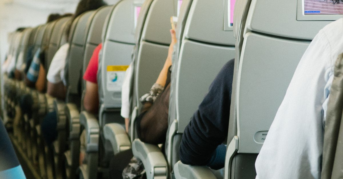 View of passengers seated in an airplane cabin, focusing on seatbacks and screens.