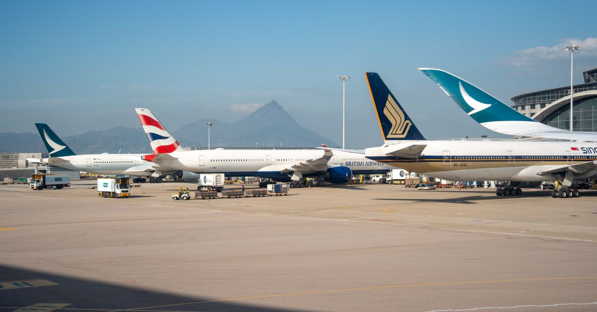 Multiple commercial airplanes parked at an airport terminal with a mountain view in the background.