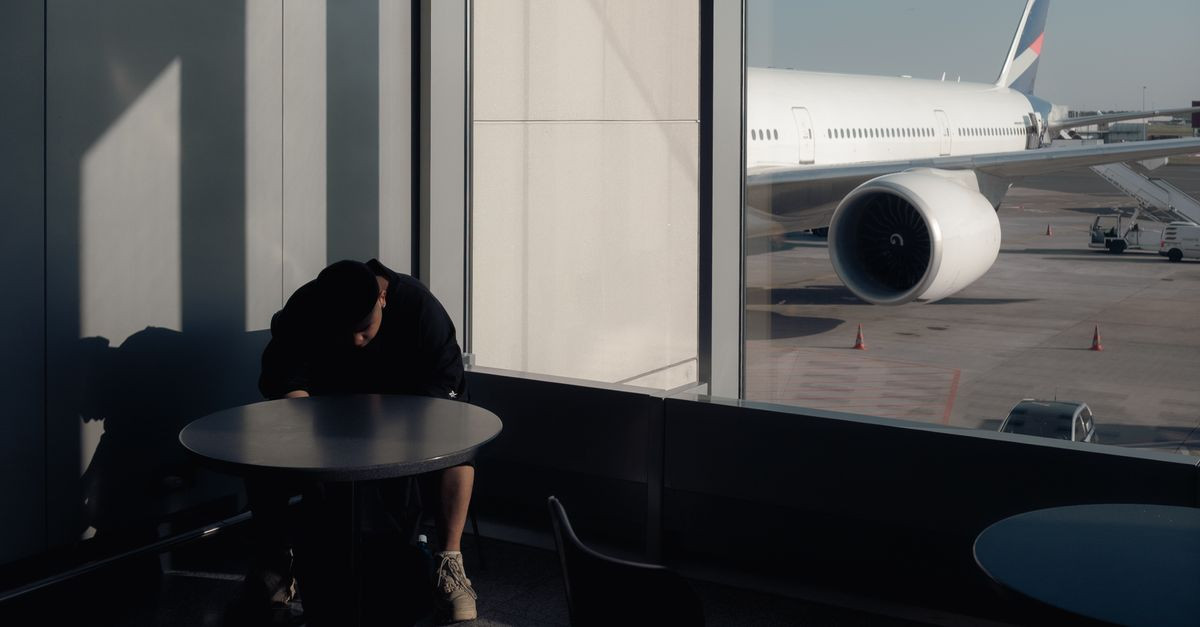 Person sitting at airport terminal window with airplane view.