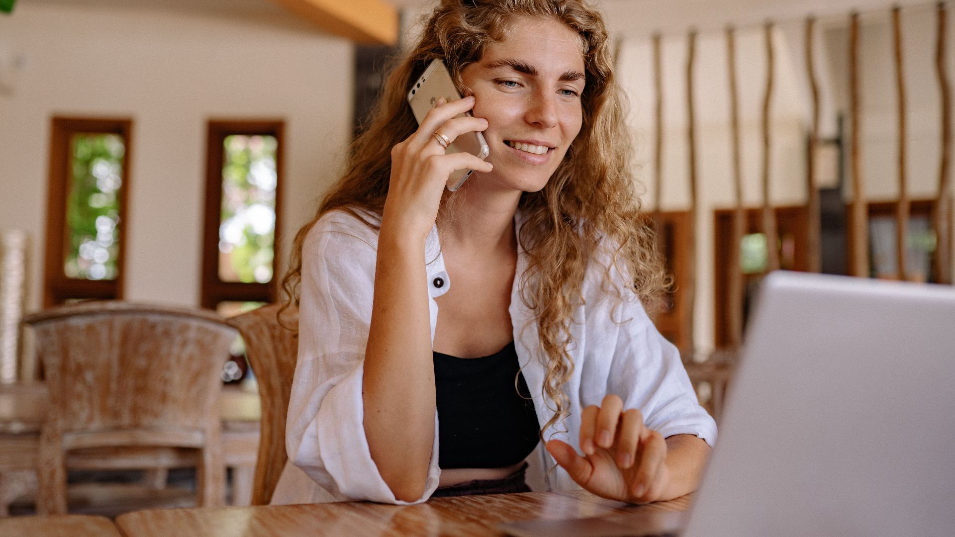 Smiling woman working remotely with a laptop and phone in a cozy setting.