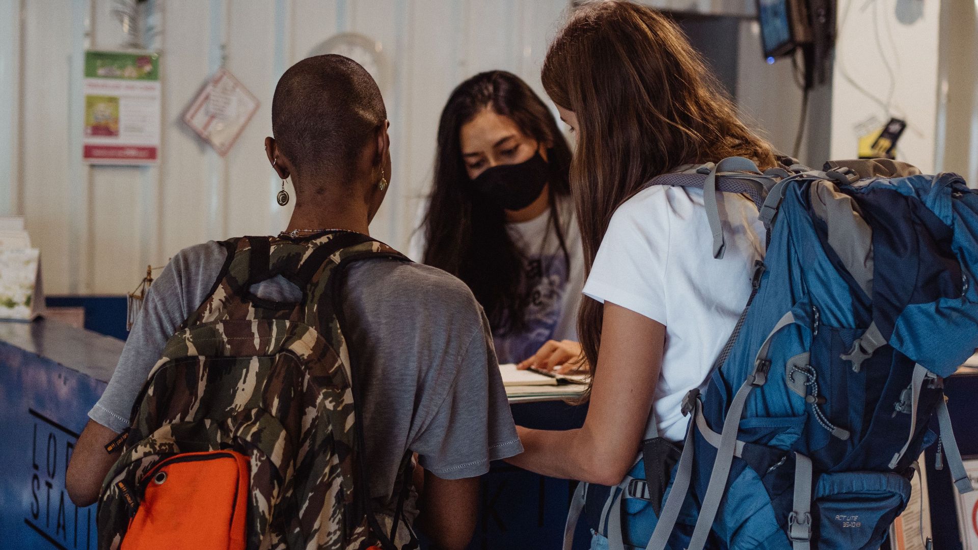 Two travelers with backpacks check in at a hostel reception counter.