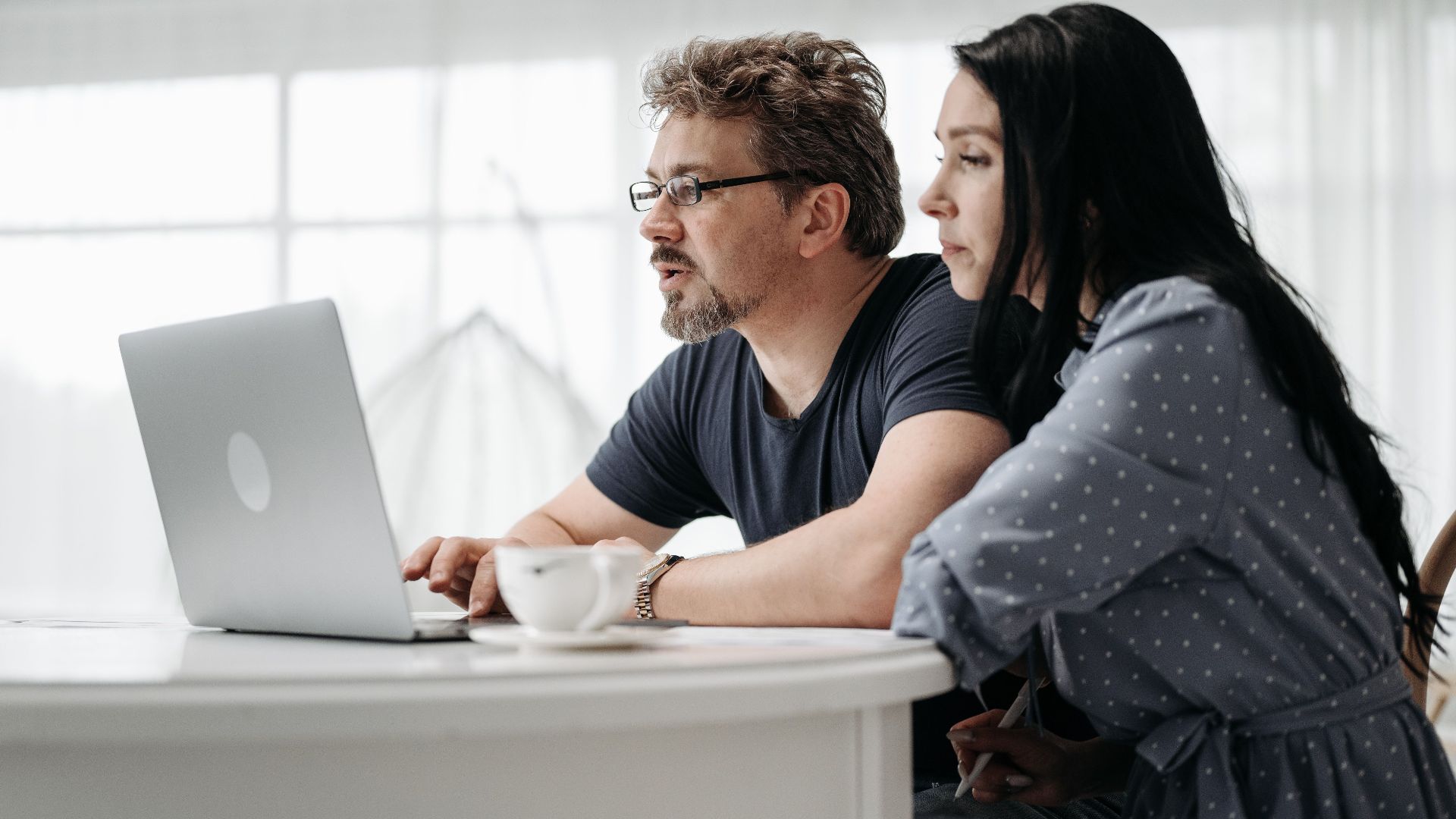 A couple uses a laptop at home in a bright and cozy setting, collaborating closely.