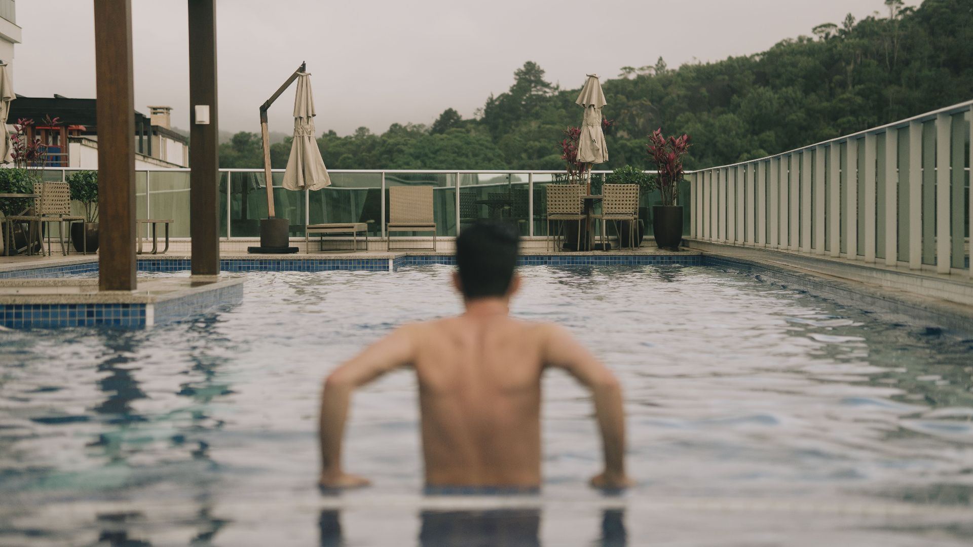 A man enjoys a refreshing swim in a rooftop pool with scenic green views.