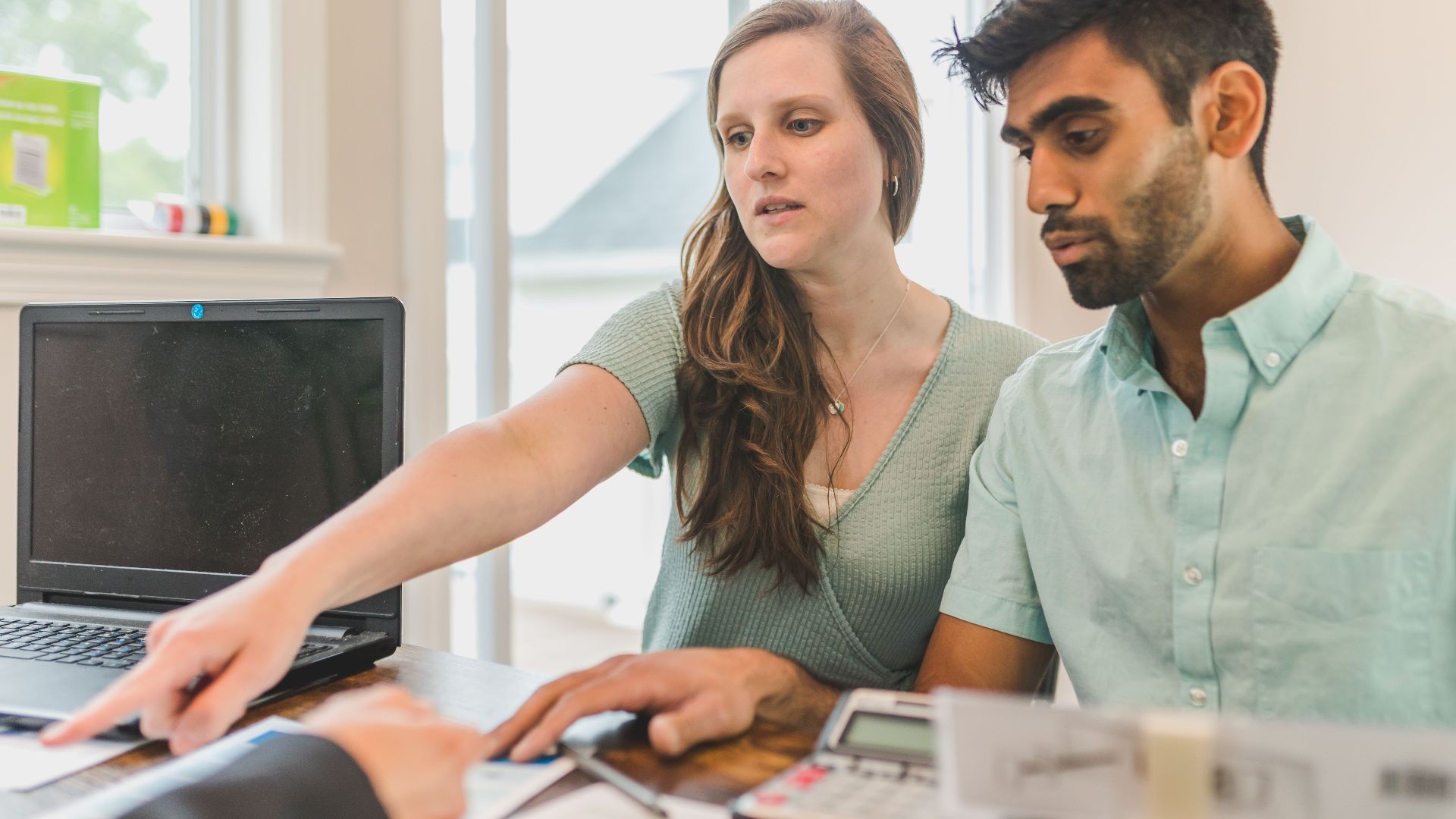 A young couple reviewing real estate documents with an advisor in a bright office.