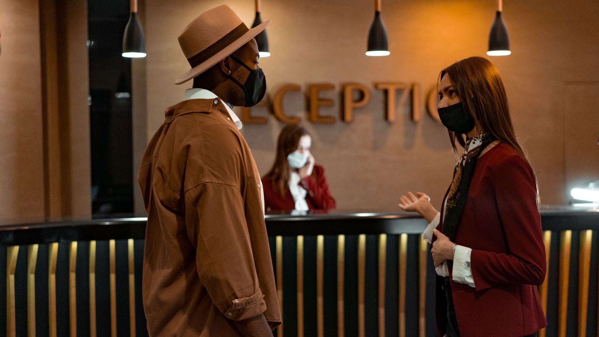 Two people in face masks interacting at a hotel reception desk during the COVID-19 pandemic.