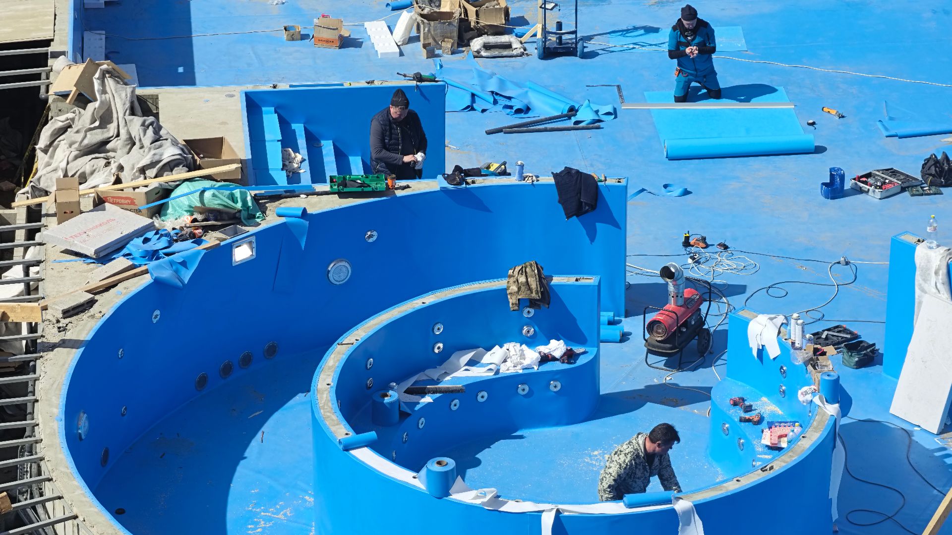 Construction workers building a new swimming pool outdoors, focus on blue interior.