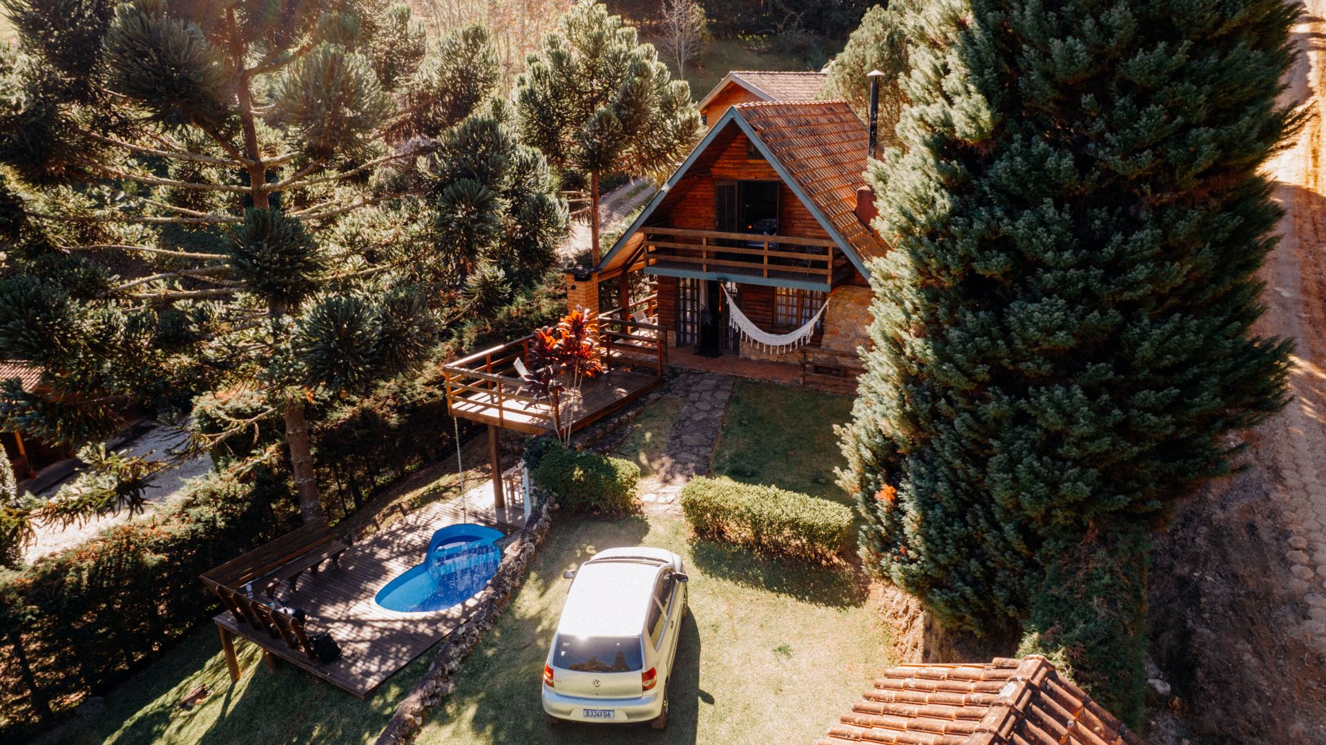 Aerial view of a cozy wooden cabin with a small pool and a car parked nearby in São Bento do Sapucaí.