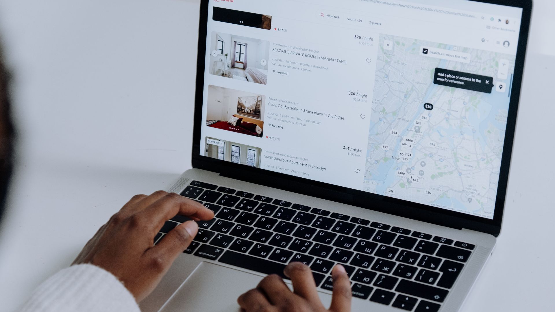 Hands typing on laptop searching Airbnb for accommodation options with map view.