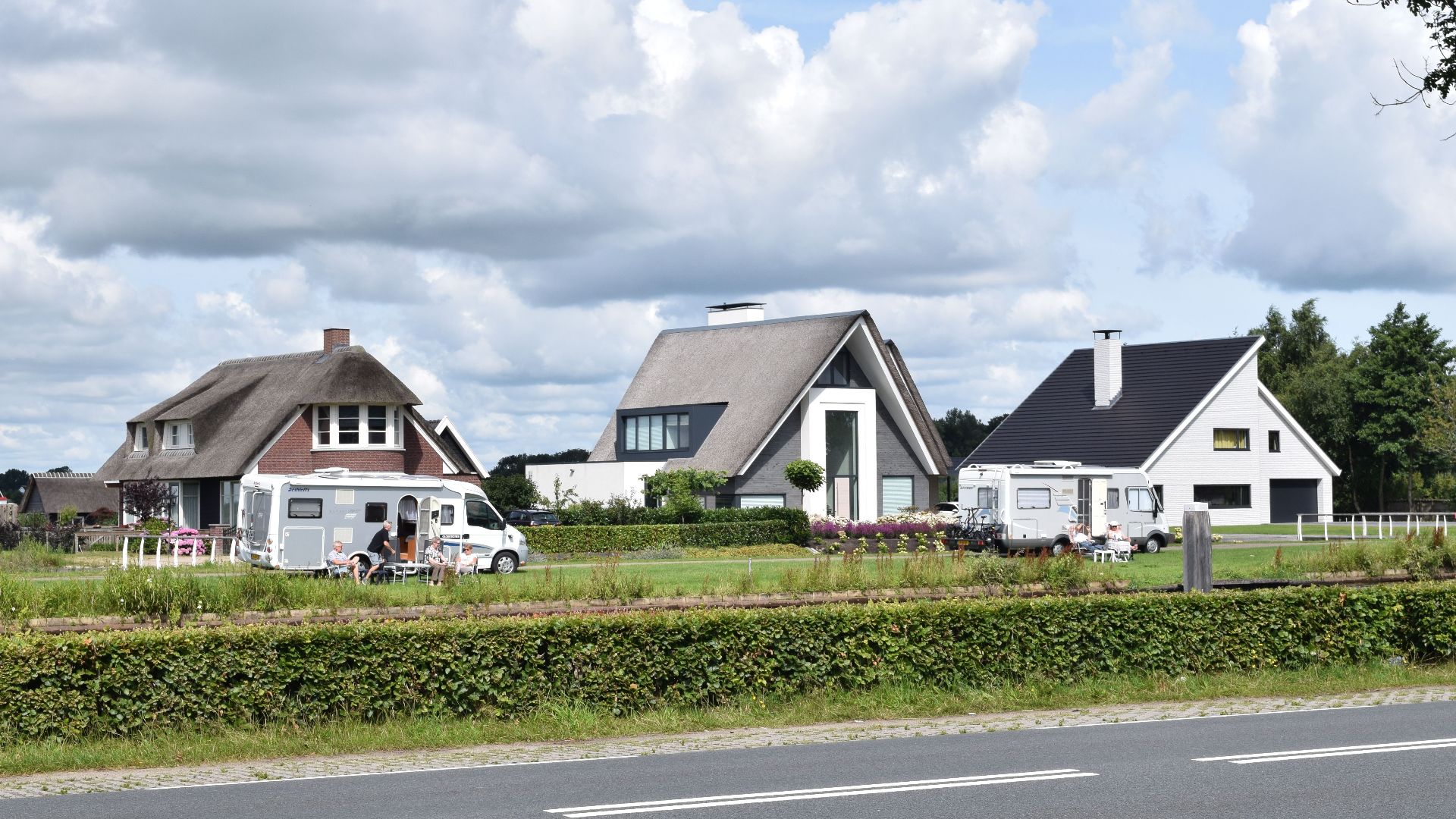 Empty asphalt road with fence and row of country houses under blue sky with clouds