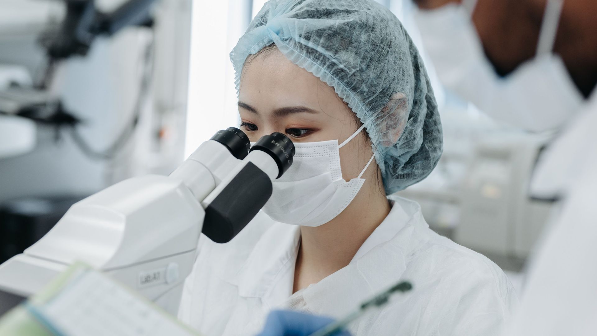 Two scientists in protective gear performing research with a microscope in a modern laboratory.