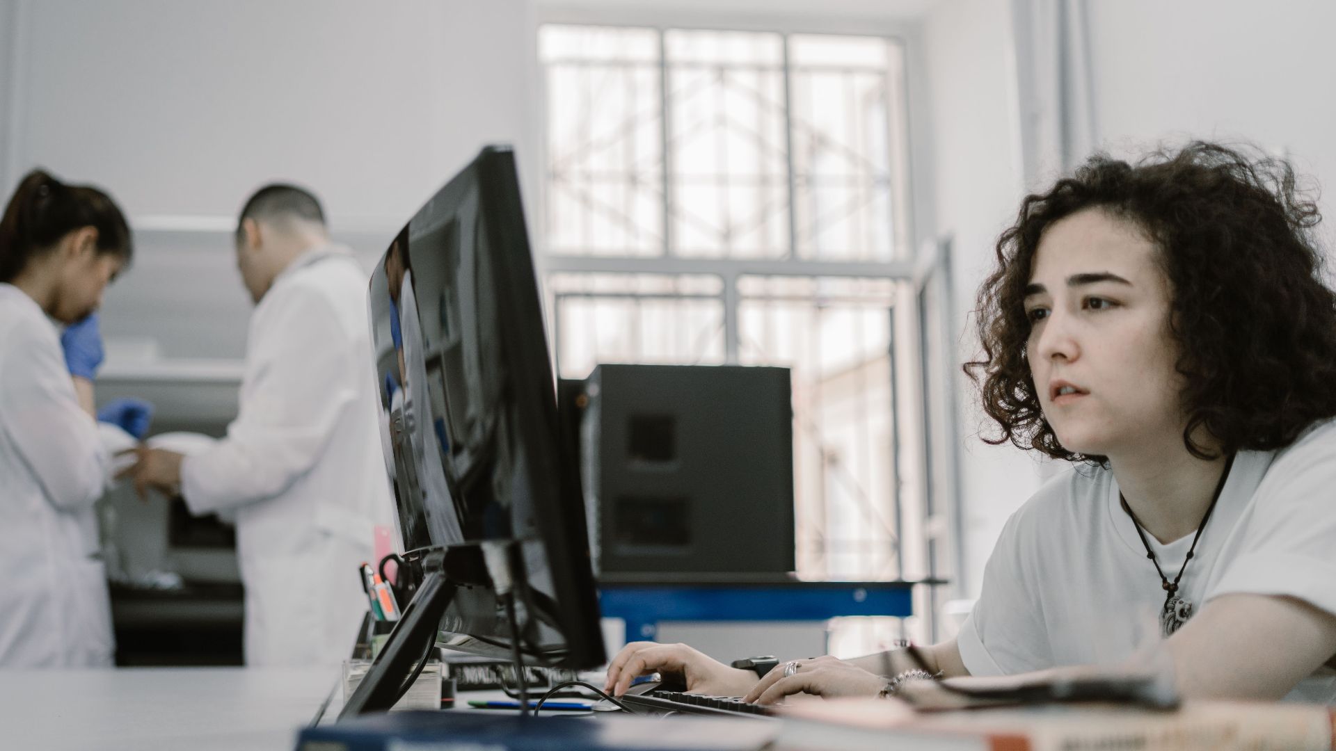 Focused woman working on a computer in a busy laboratory setting, showcasing teamwork and scientific research.