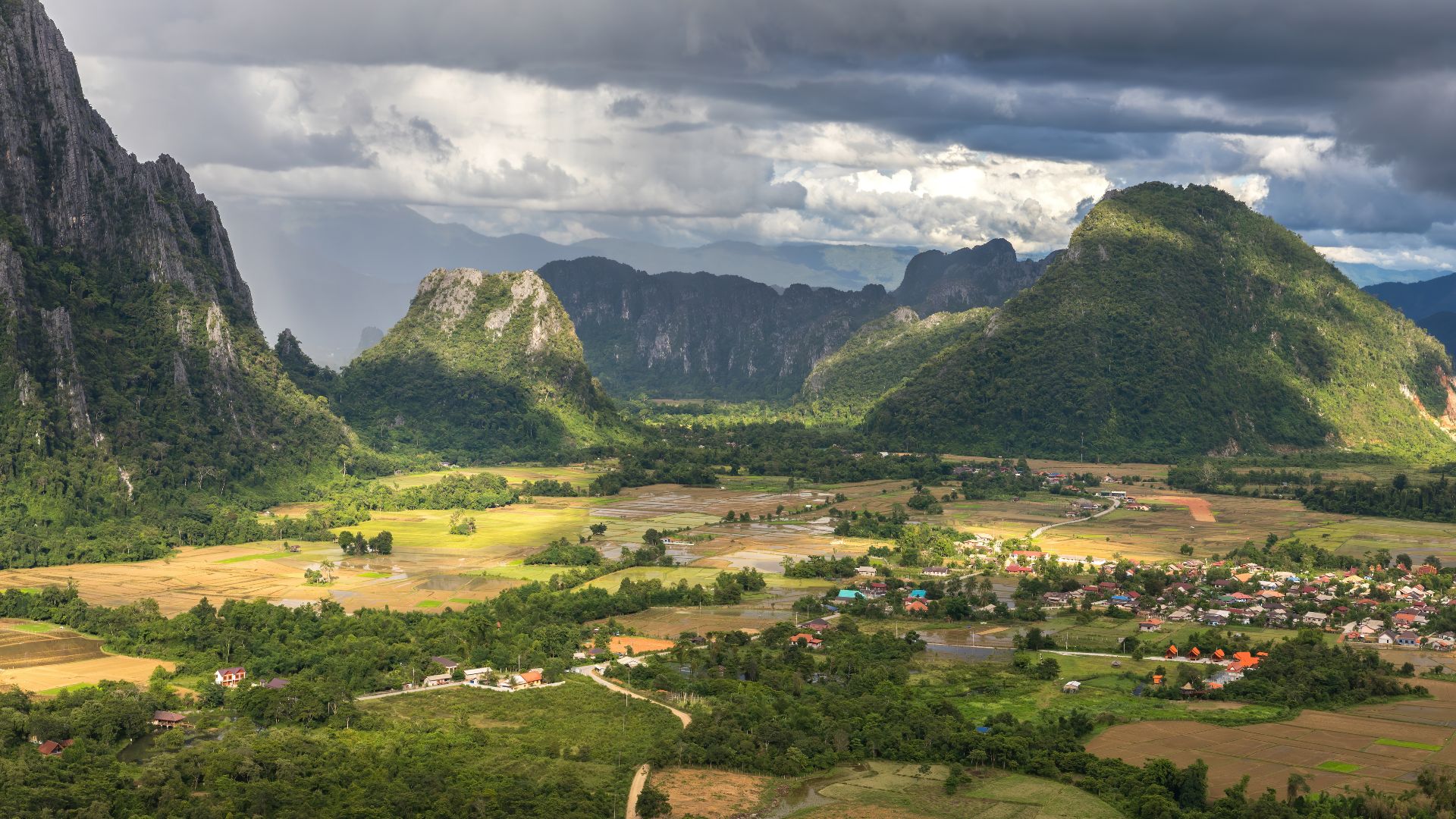 Karst peaks and green paddy fields under a stormy sky, South view from the top of Mount Nam Xay, during the monsoon, in Vang Vieng, Vientiane Province, Laos.