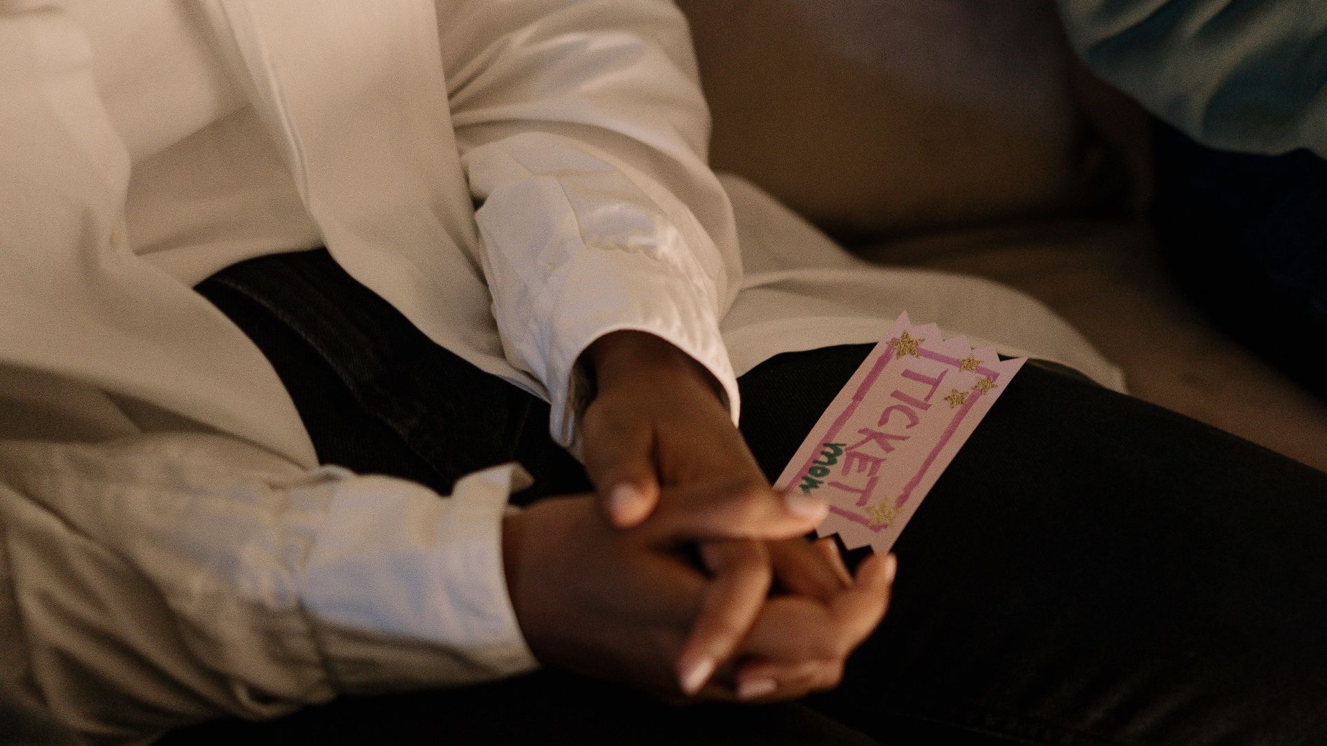 A close-up shot of hands holding a colorful ticket while sitting, conveying anticipation.