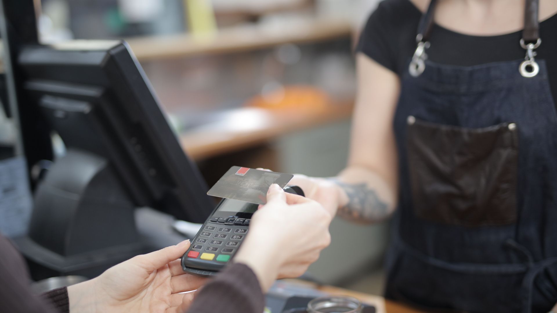 Close-up of customer and cashier during a credit card transaction at a store counter indoors.