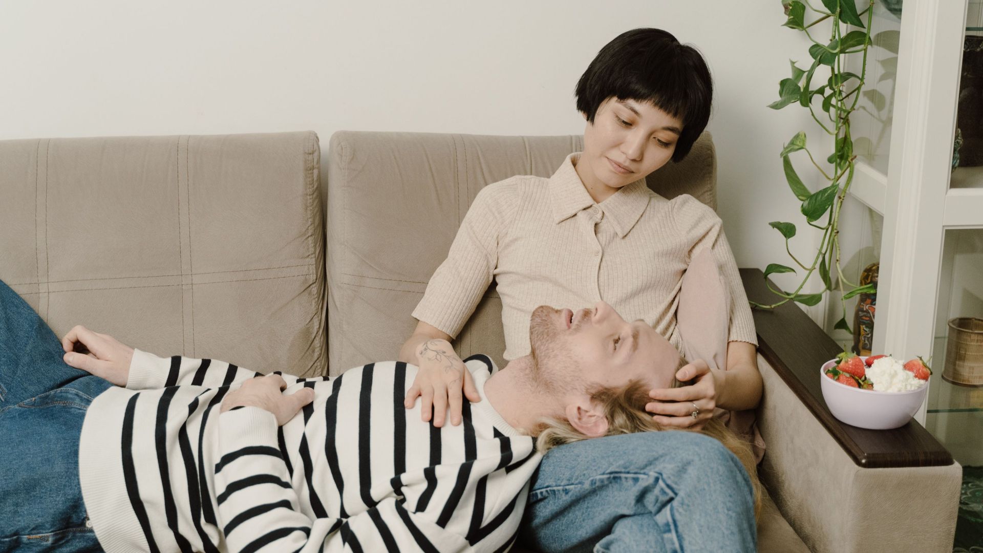 Interracial couple sitting on a sofa, enjoying a peaceful moment and sharing affection indoors.