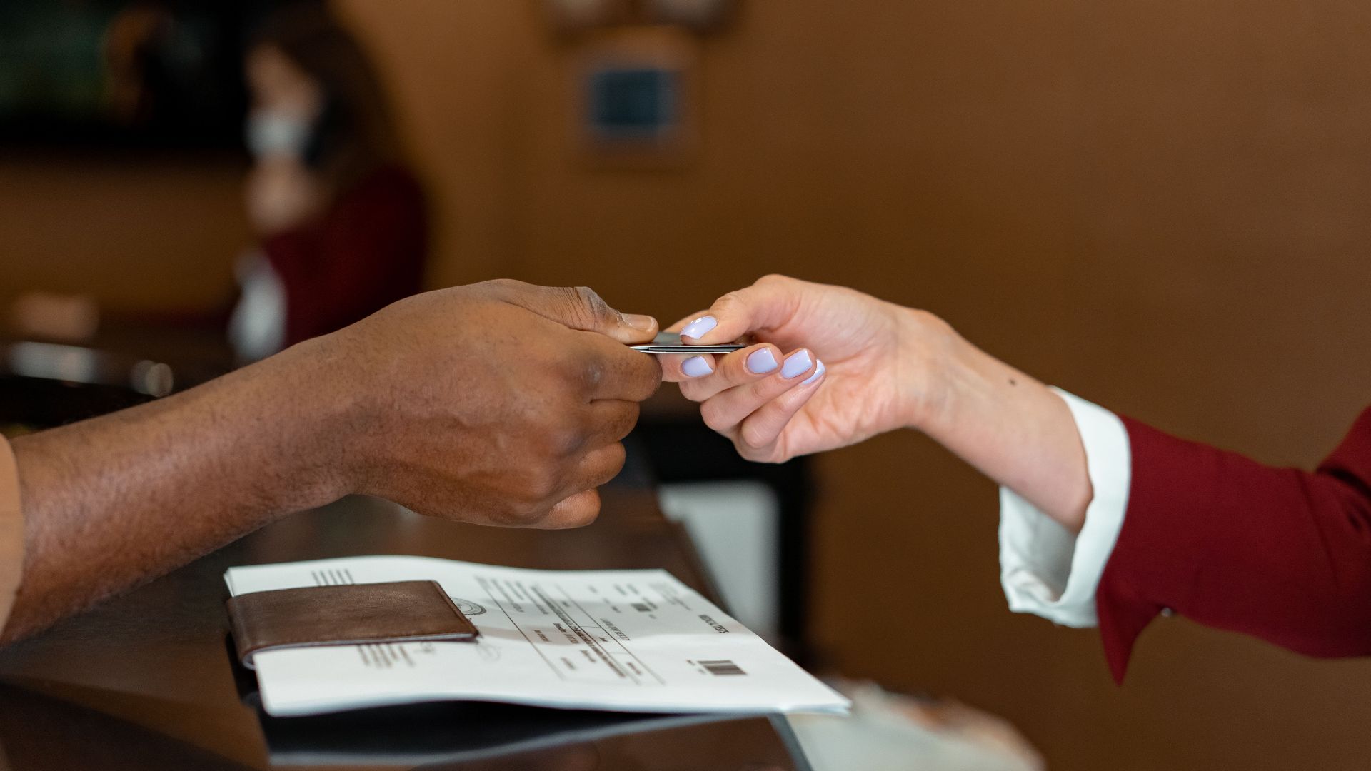 Close-up of a hotel receptionist receiving a credit card from a guest, highlighting a transaction at check-in.