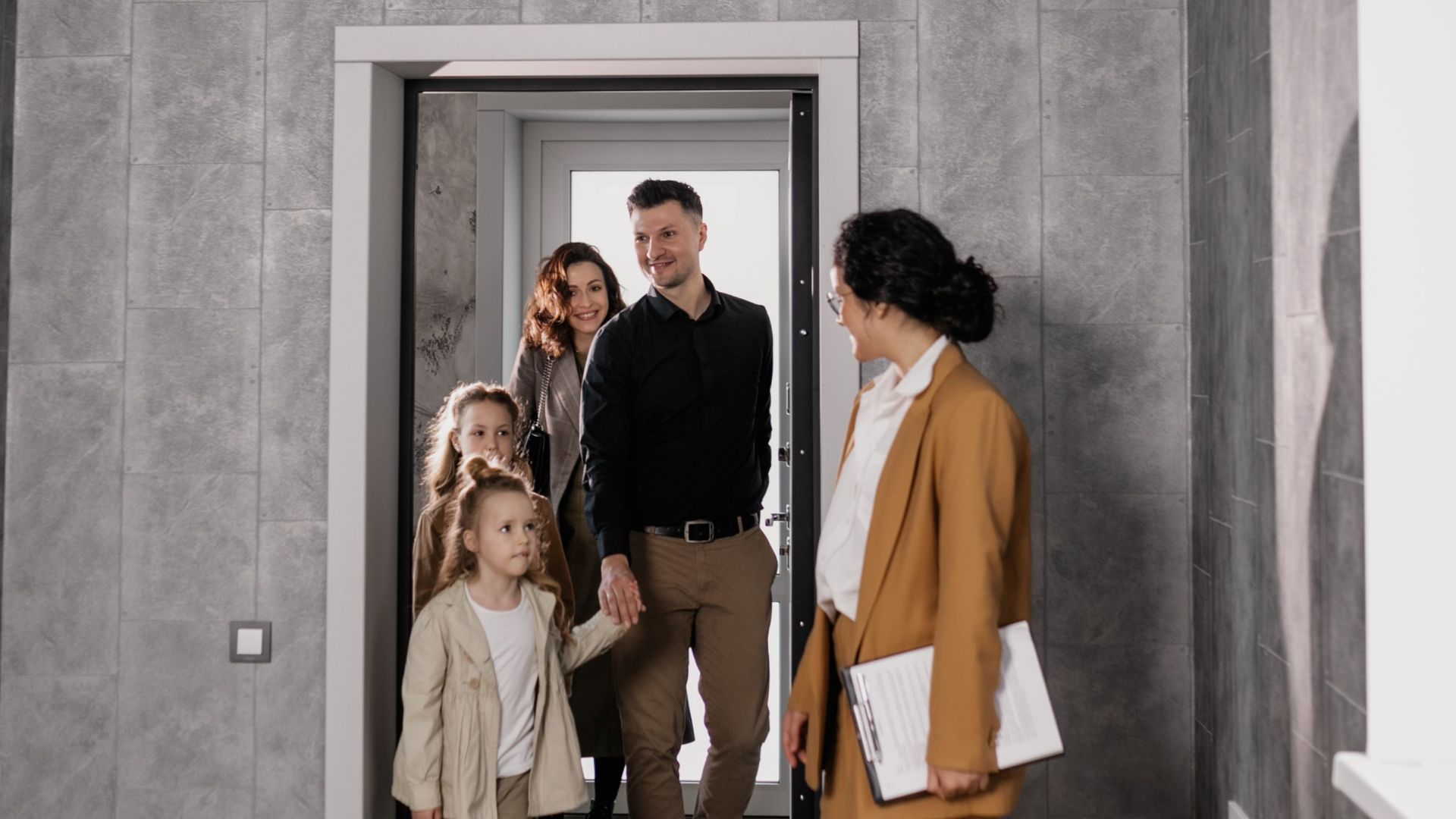 A family enters a new home with a real estate agent welcoming them inside.
