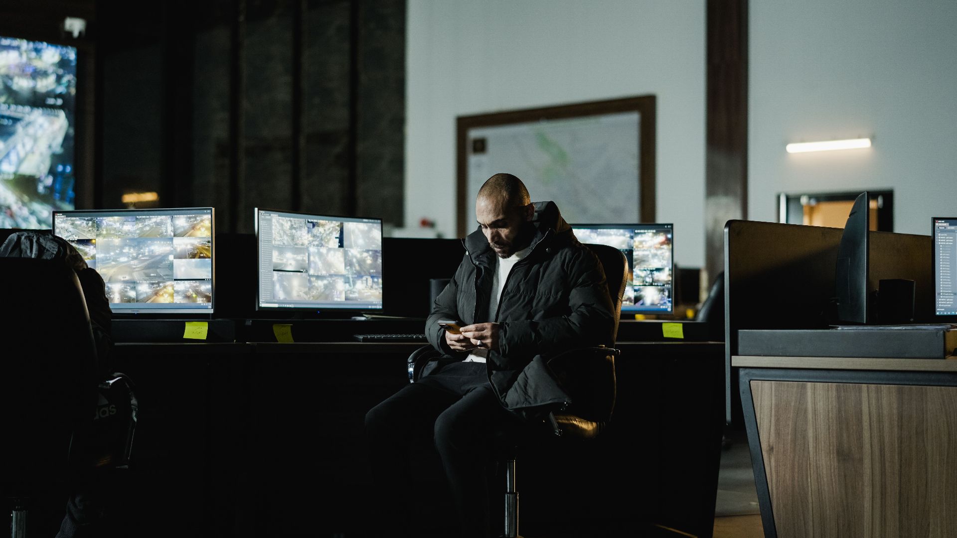 Security officer seated in a dimly lit control room, analyzing multiple surveillance screens.