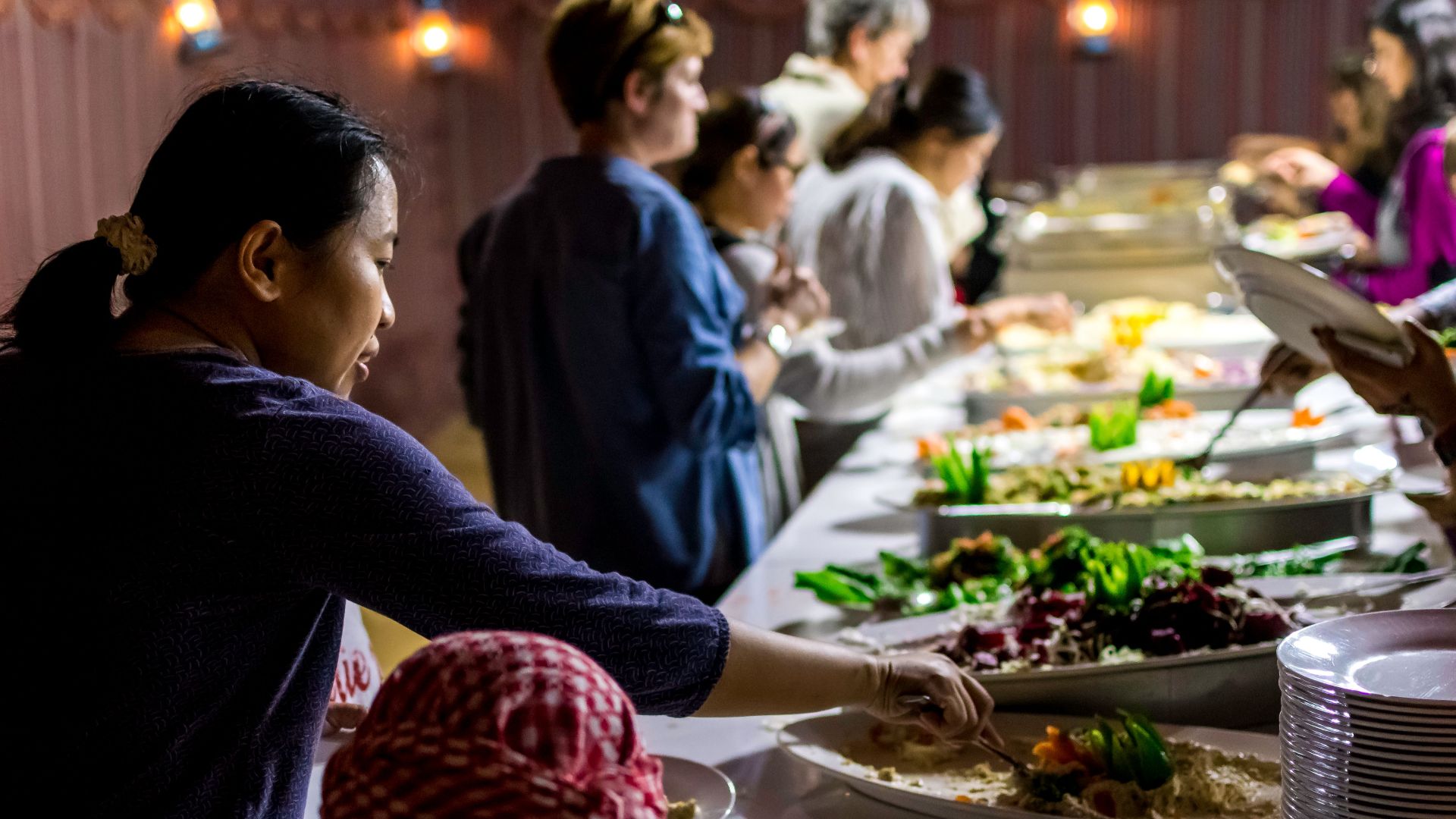A diverse group of people enjoying a buffet dinner indoors with various dishes.