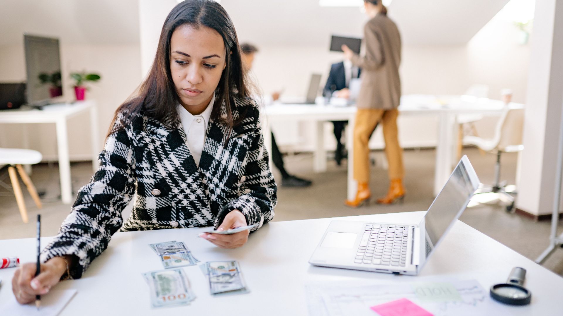 Businesswoman calculating finances with cash and a laptop in a modern office.