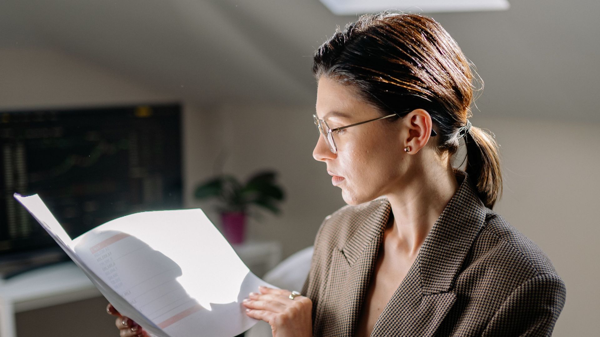 Professional woman in glasses reviewing financial documents at her office desk.