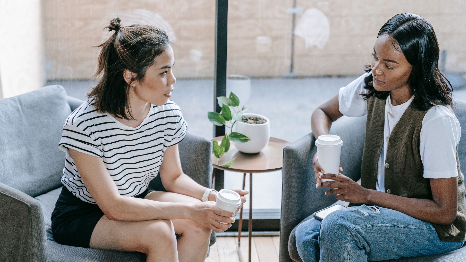 Two young women enjoying coffee and conversation indoors in a cozy setting.