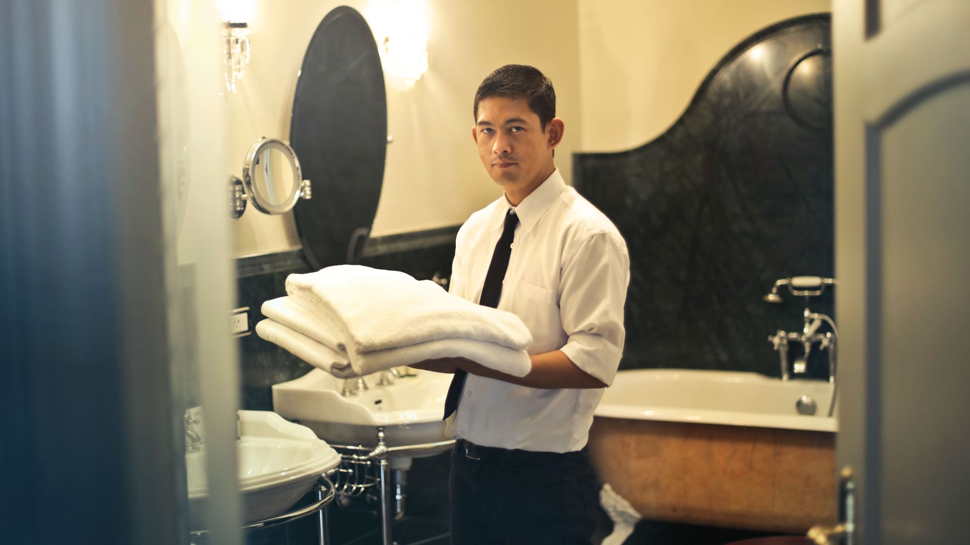 A hotel employee holding towels in a luxury bathroom with elegant decor.