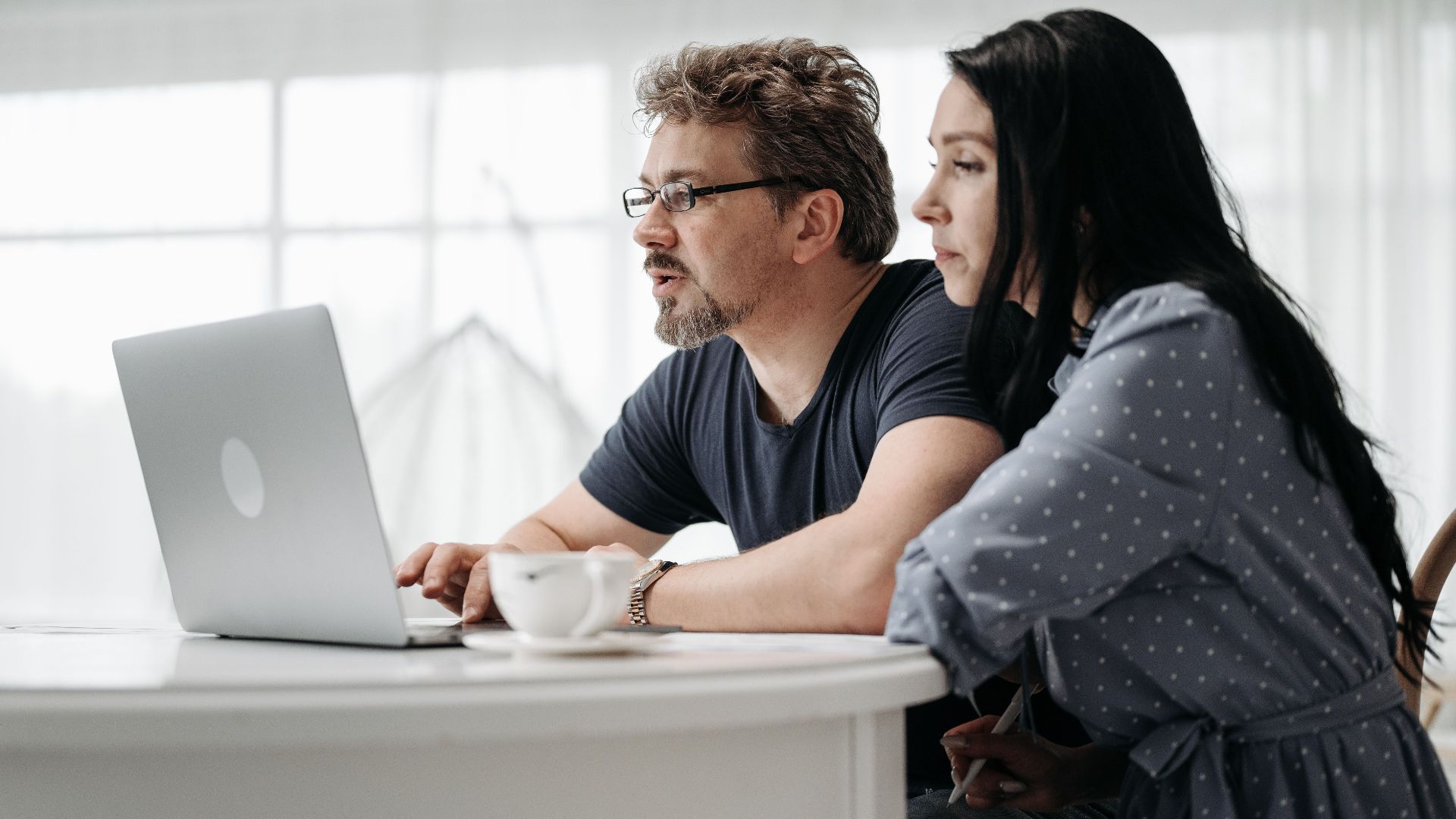 A couple uses a laptop at home in a bright and cozy setting, collaborating closely.
