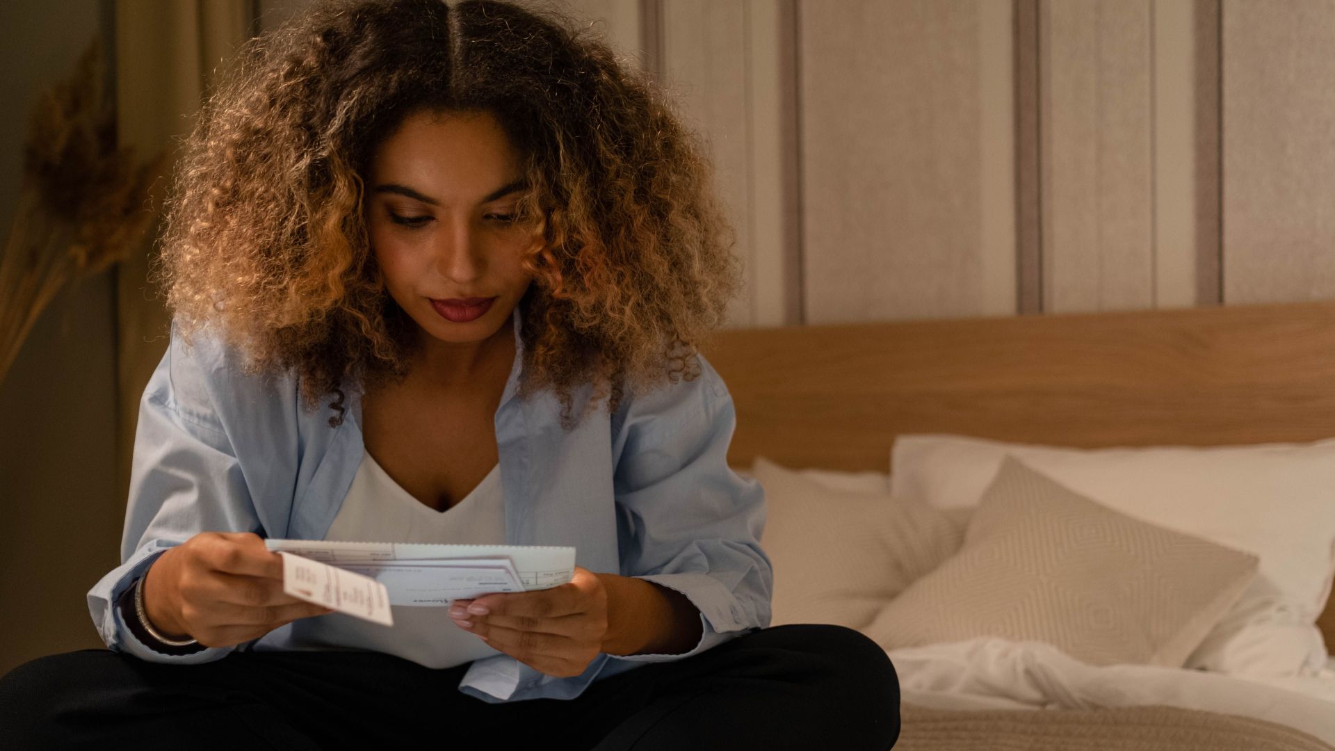 Woman sitting on bed reading documents with laptop, highlighting home office setting.