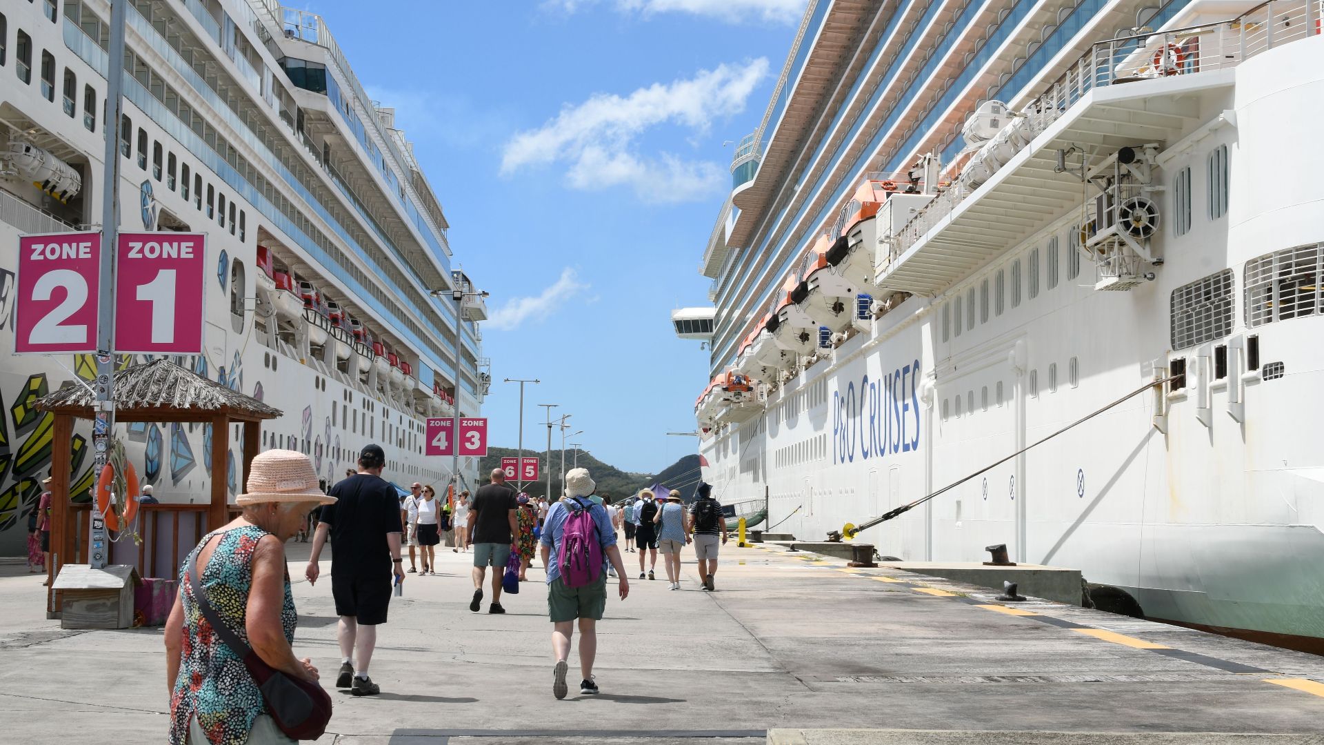 Bustling cruise port with tourists, featuring two large cruise ships under a bright blue sky.