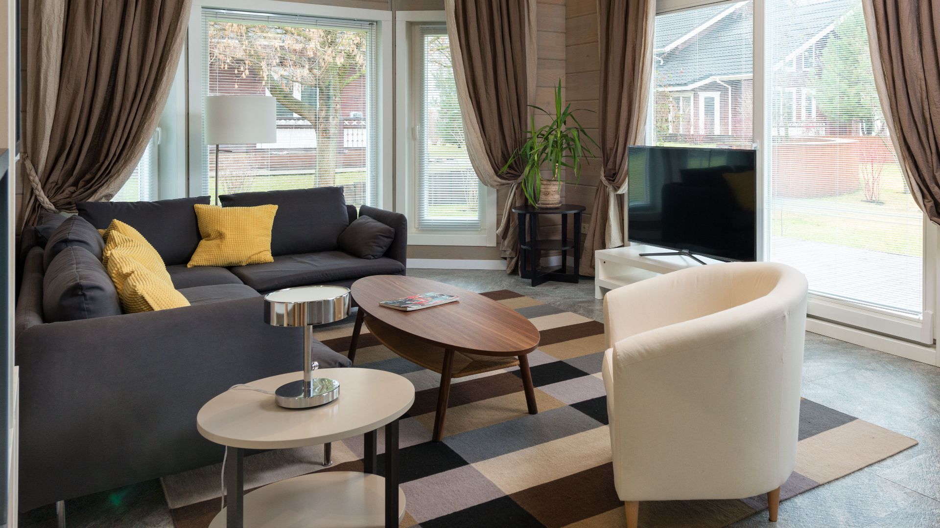 Comfortable corner sofa with cushions placed near round wooden table and armchair in living room equipped with TV set