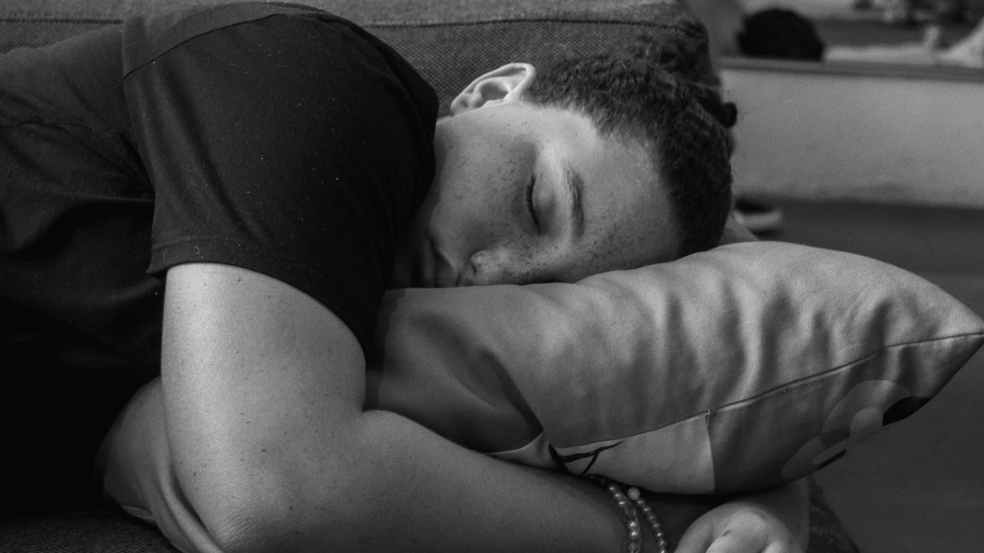 A person peacefully sleeping on a sofa, resting their head on a pillow in a black and white setting.