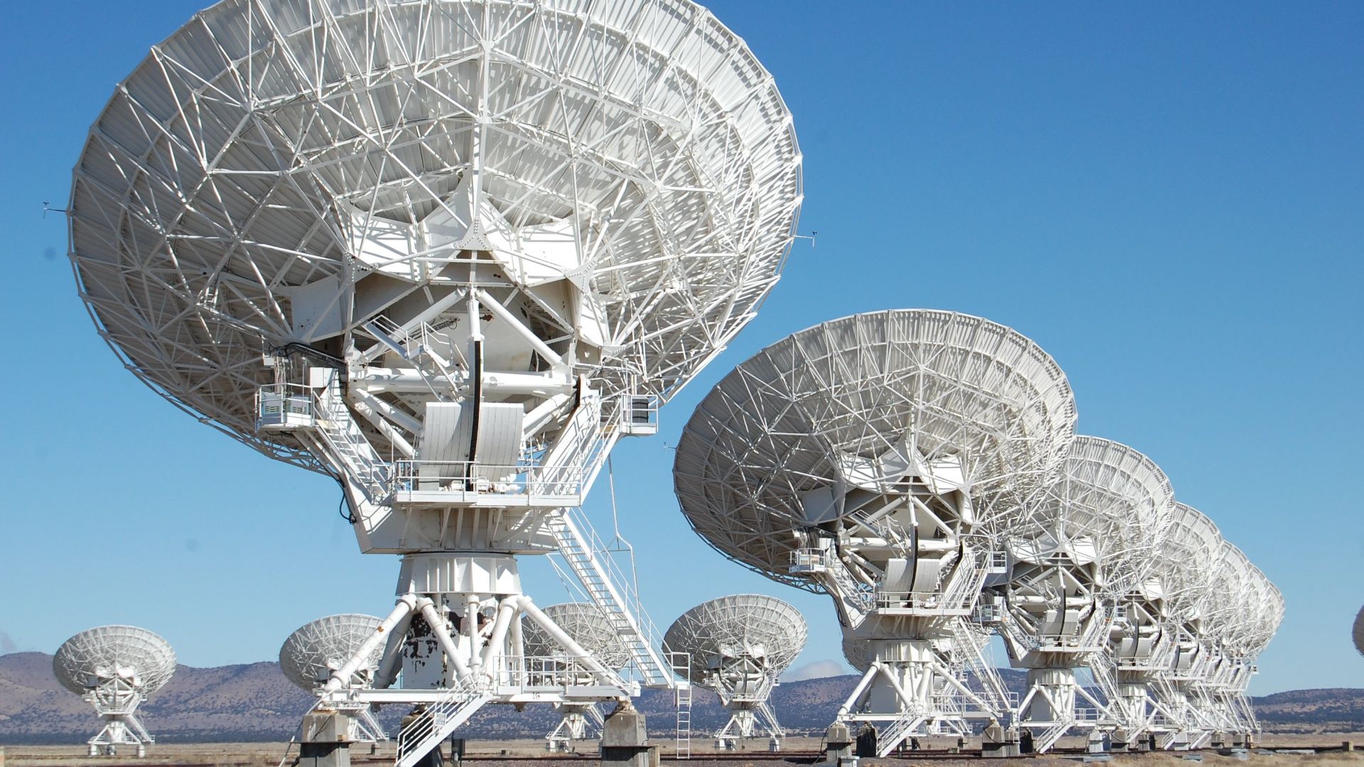 Array of radio telescopes at the Very Large Array in New Mexico under a clear blue sky.
