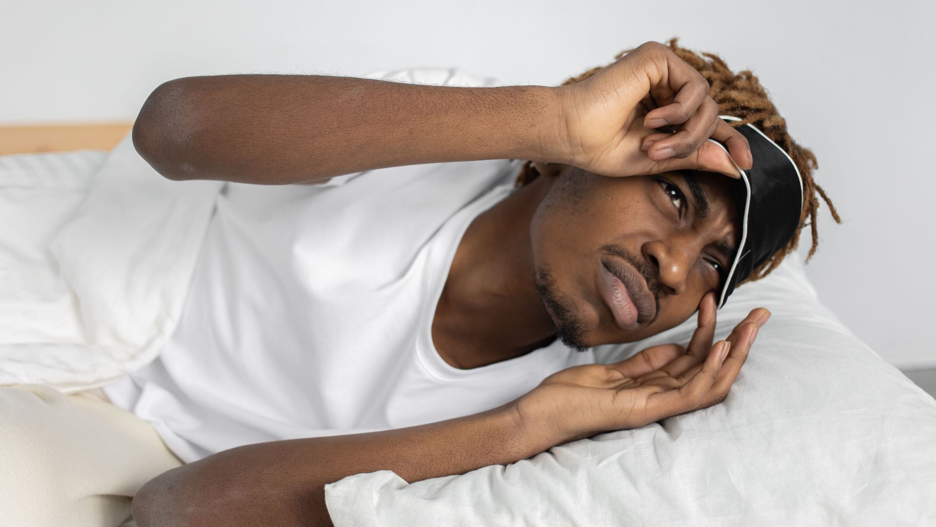 Young man removes sleep mask, starting his day in bed, indoors.