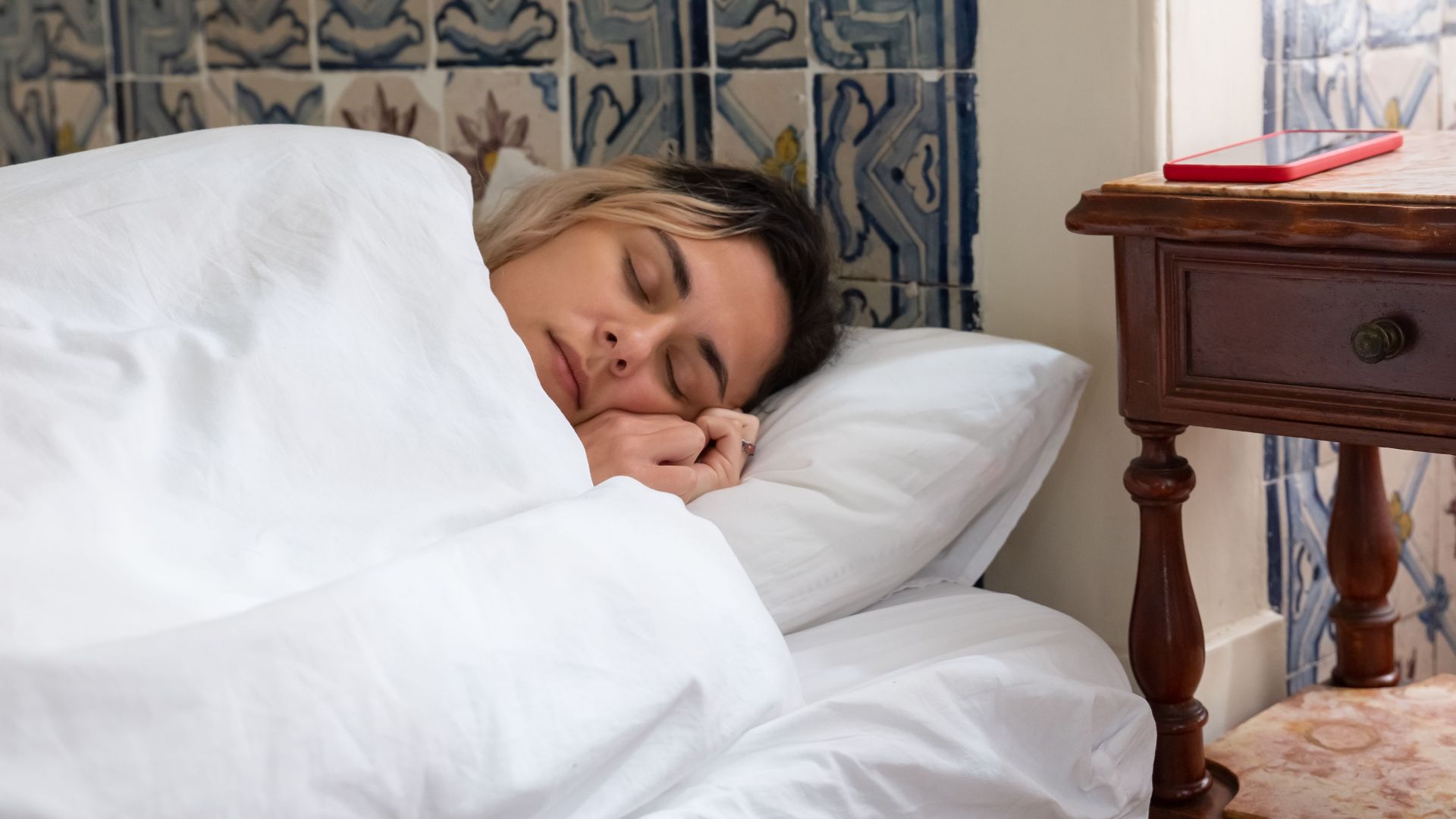 A woman sleeping soundly in a bed with traditional Portuguese tiles in the background.