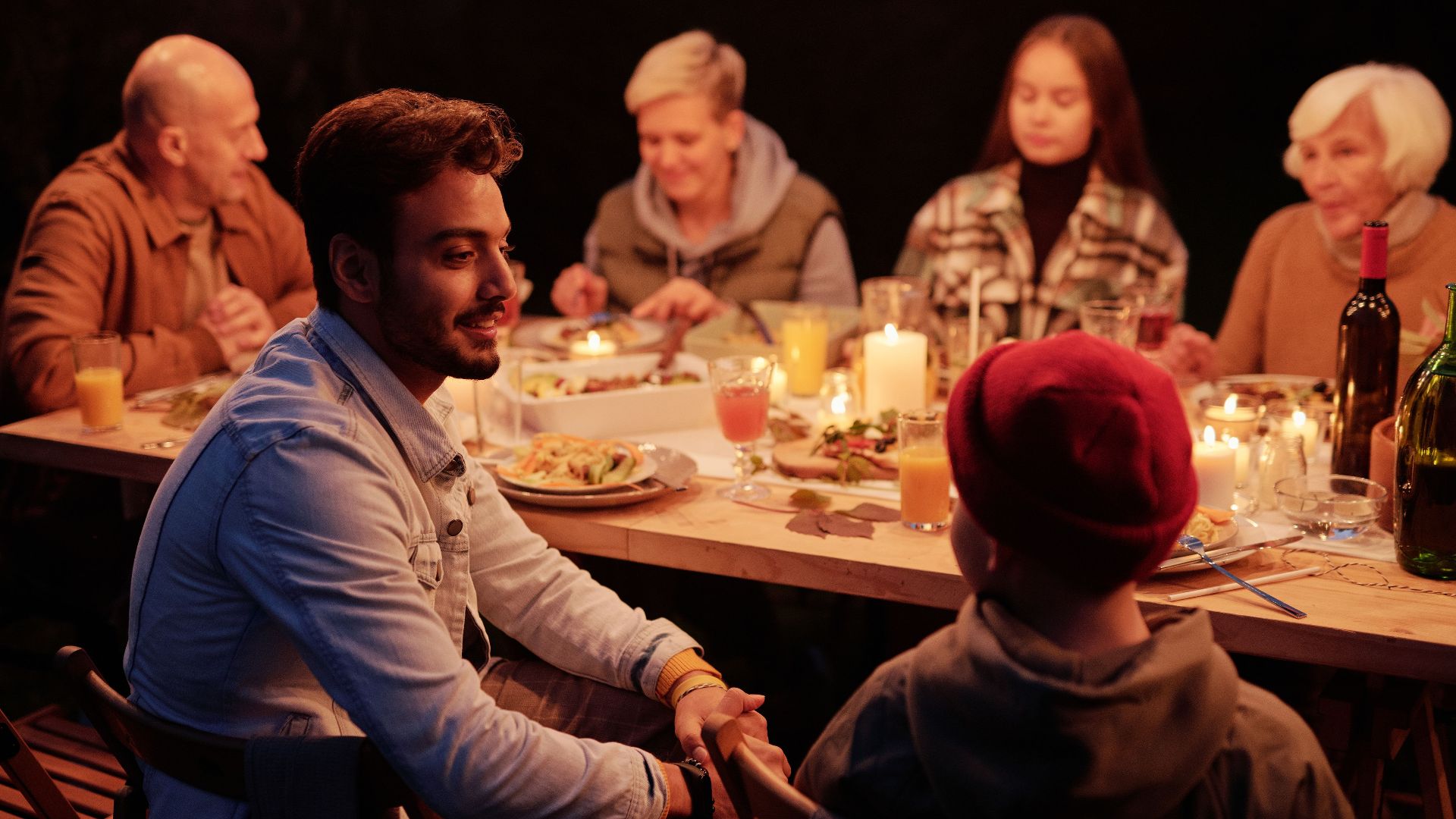 Smiling Indian man and boy chatting at festive table with family and friends during reunion