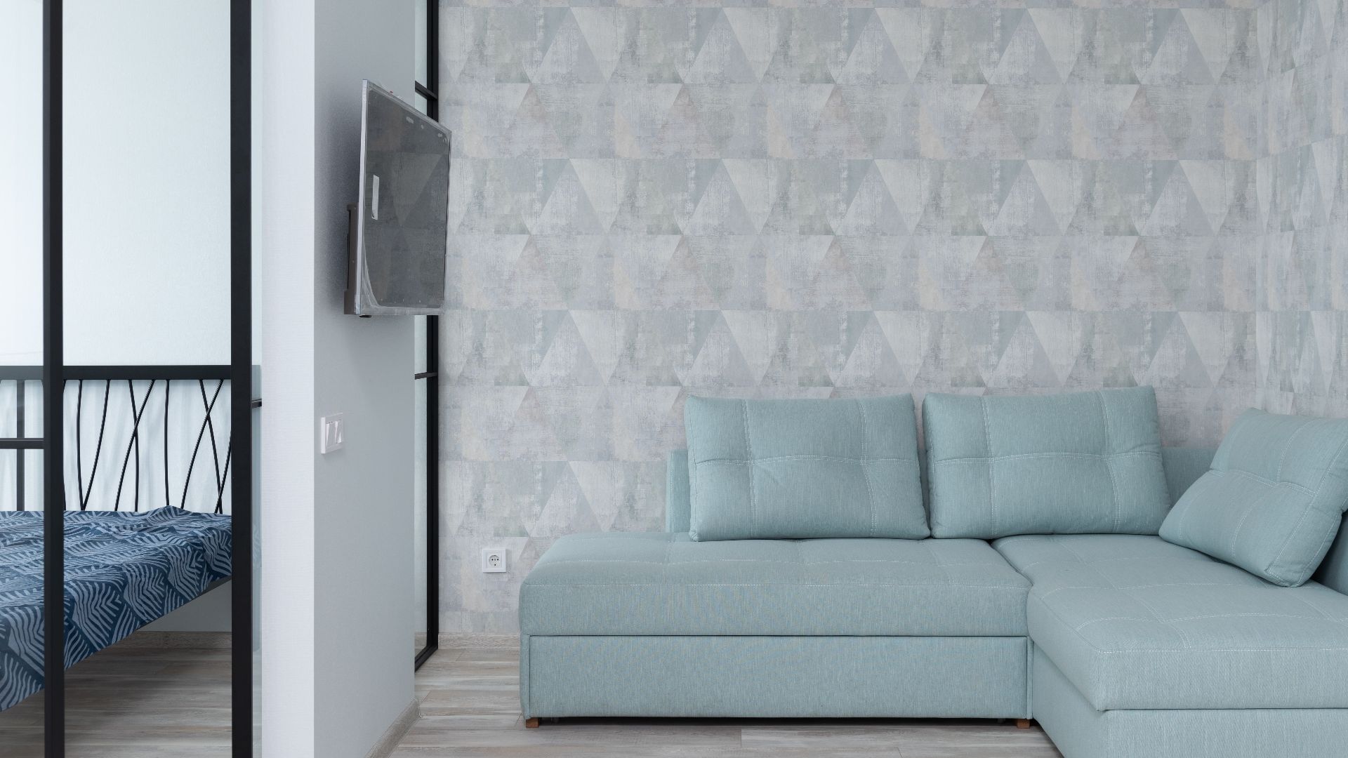 Interior of stylish flat with comfortable sofa with cushions placed near wall with wallpaper near bedroom with bed at home