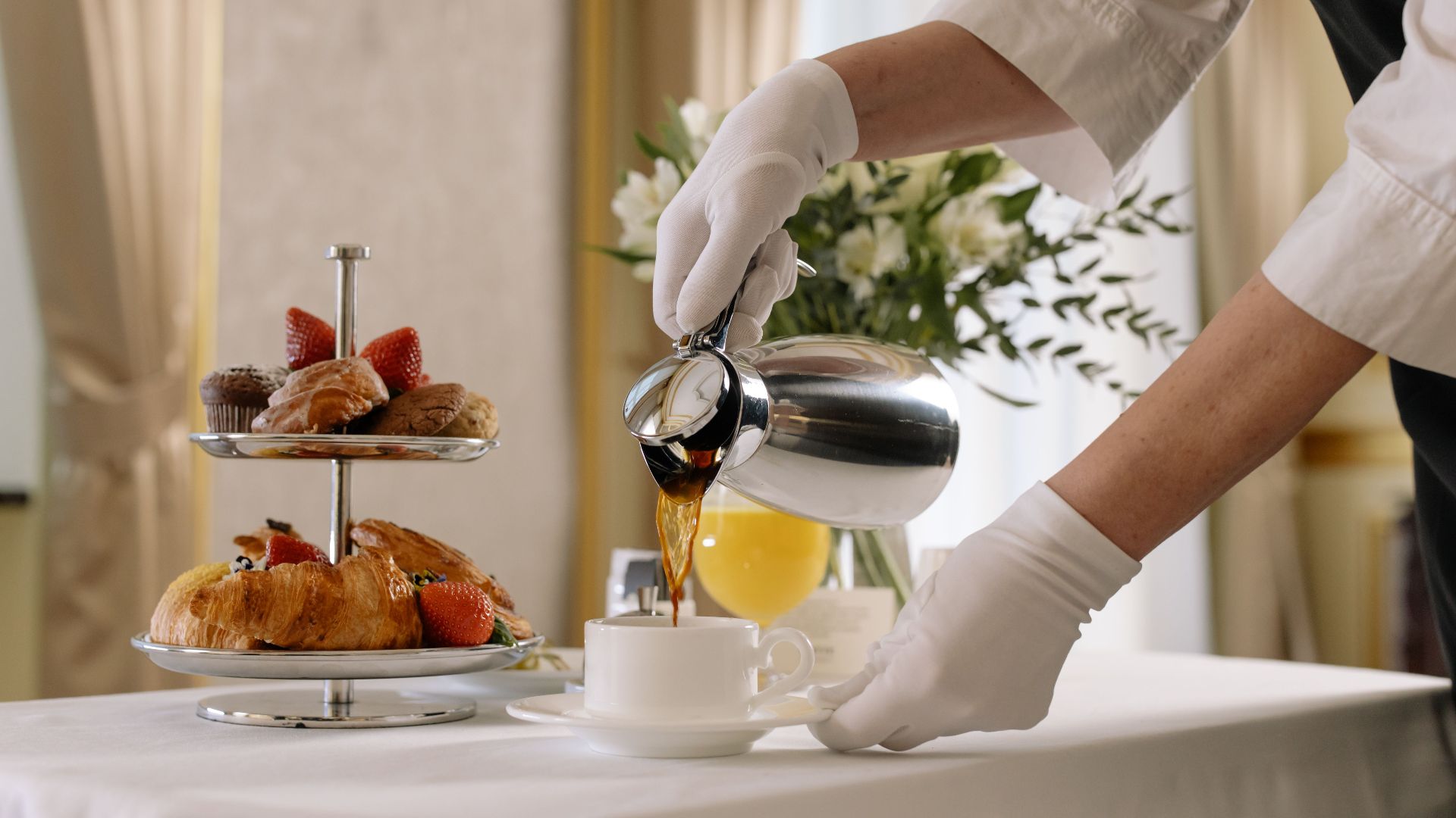 Luxurious breakfast scene with fresh pastries, coffee being poured, and elegant table setting.