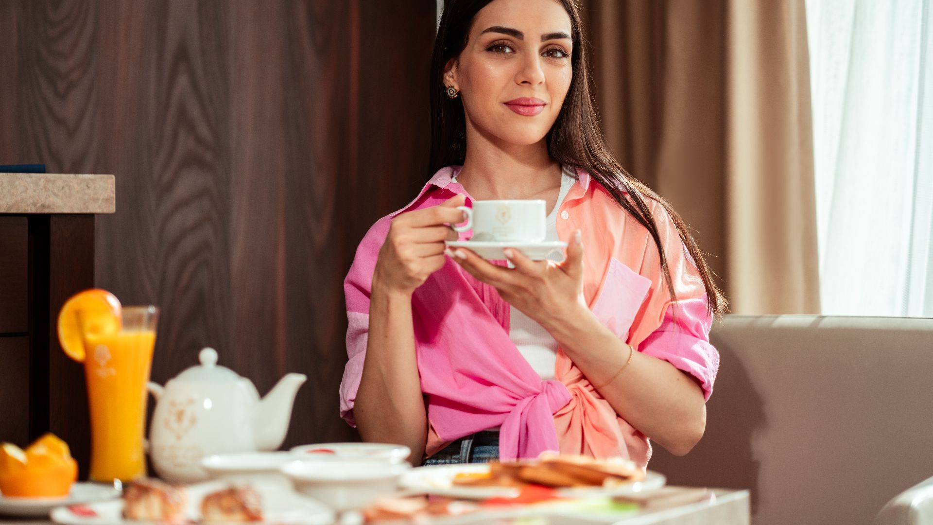 Woman enjoying a leisurely breakfast indoors with tea and juice in Baghdad hotel.