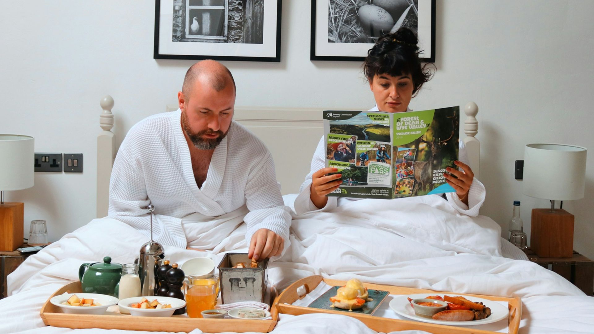 a man and woman sitting on a bed reading a magazine
