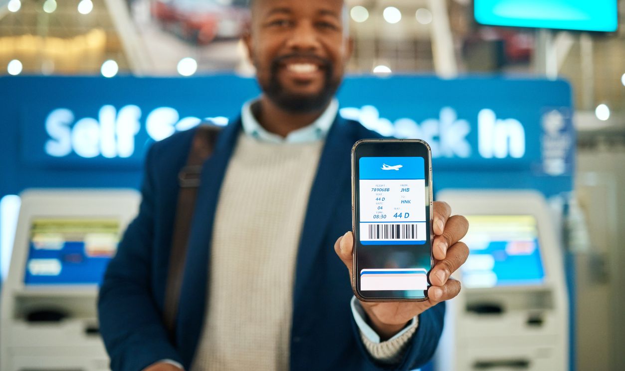Shutterstock - 2262323387 - Airport, travel and man with a boarding pass on his phone to check in before his flight for a work trip. Technology, professional and African business male with a electronic plane ticket on cellphone.