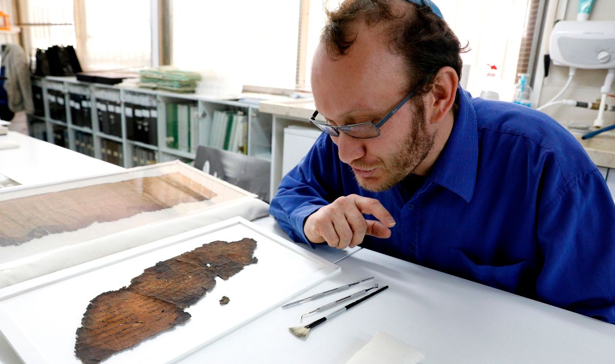Oren Ableman, a Dead Sea scrolls researcher of the Israel Antiquities Authority (IAA) -- who examined scroll fragments with the aid of advanced imaging equipment and revealed a previously unseen script -- looks at a large scroll fragment at the conservation laboratory of the IAA in Jerusalem on May 2, 2018. - The Dead Sea Scrolls are a collection of hundreds of biblical texts in Hebrew, Aramaic, and Greek discovered 45 years ago in the Qumran Caves near the Dead Sea.